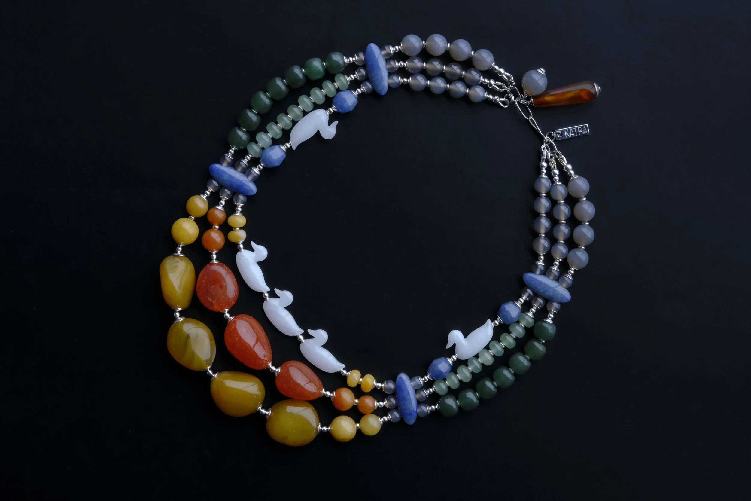 Colorful beaded necklace with laser-cut duck-shaped quartz beads and elongated aventurine oval connectors on a black background.