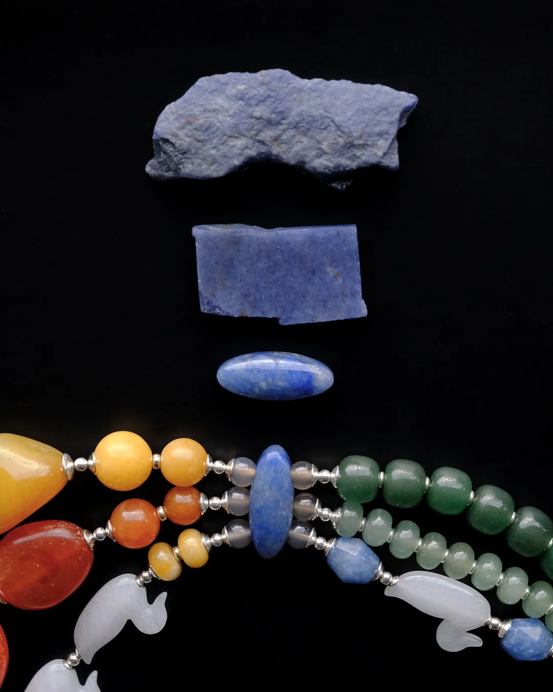 Aventurine rough piece, a slab and a laser-cut aventurine bead with a colorful beaded necklace with duck-shaped quartz beads on a black background.