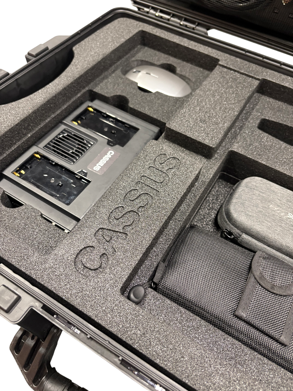 Open black carrying case with foam insert labeled 'C.A.S.S.' containing electronic components, including a white computer mouse and a gray hard case.