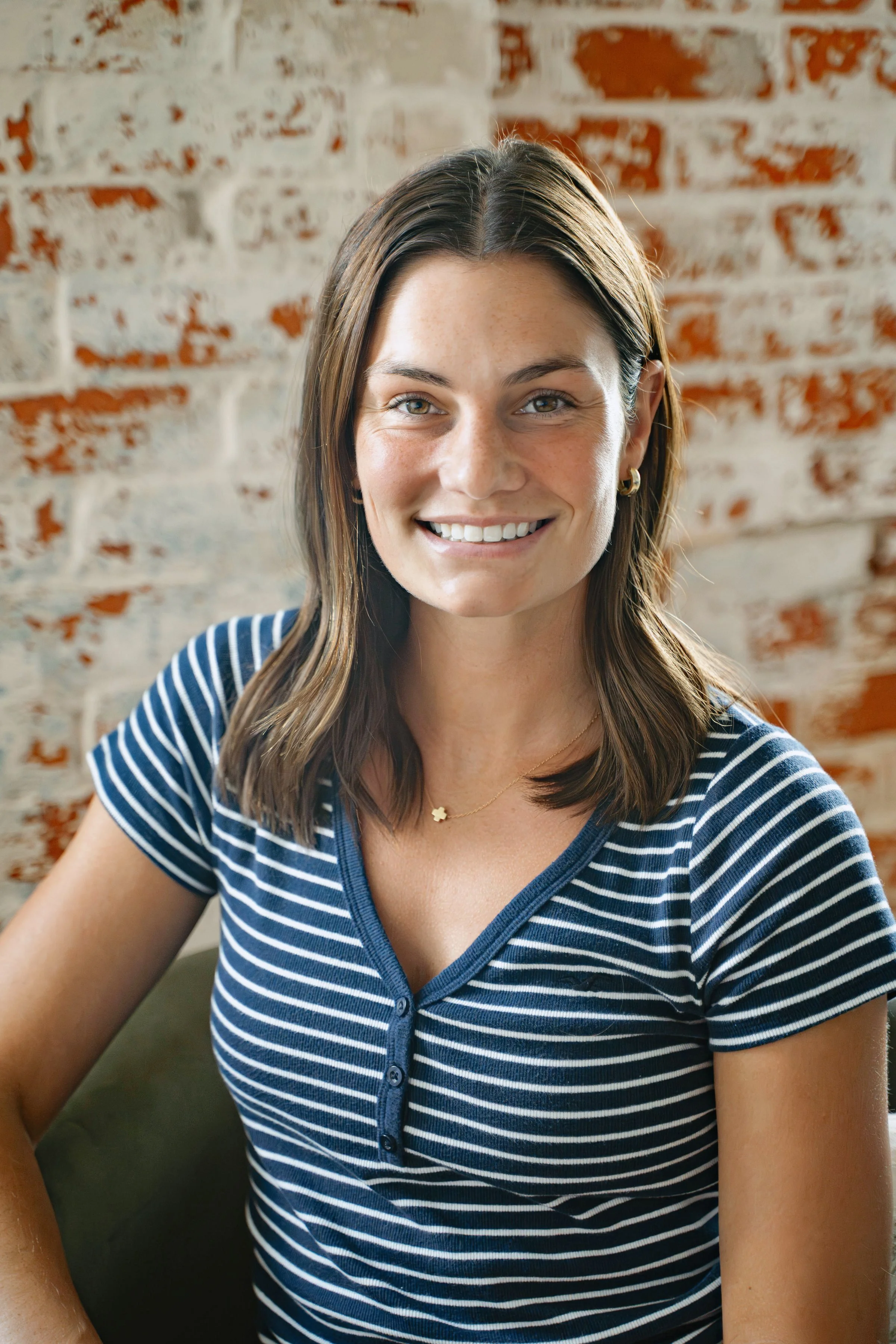 A person sitting on a couch wearing a white sweater with black stripes. There is a plant and a brick wall in the background.