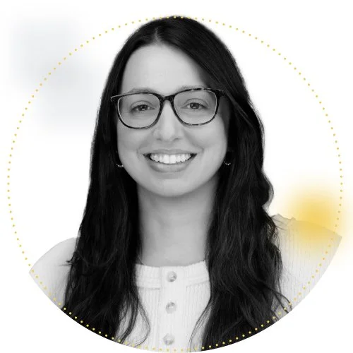 Black and white portrait of a woman with wavy hair wearing glasses, smiling at the camera.