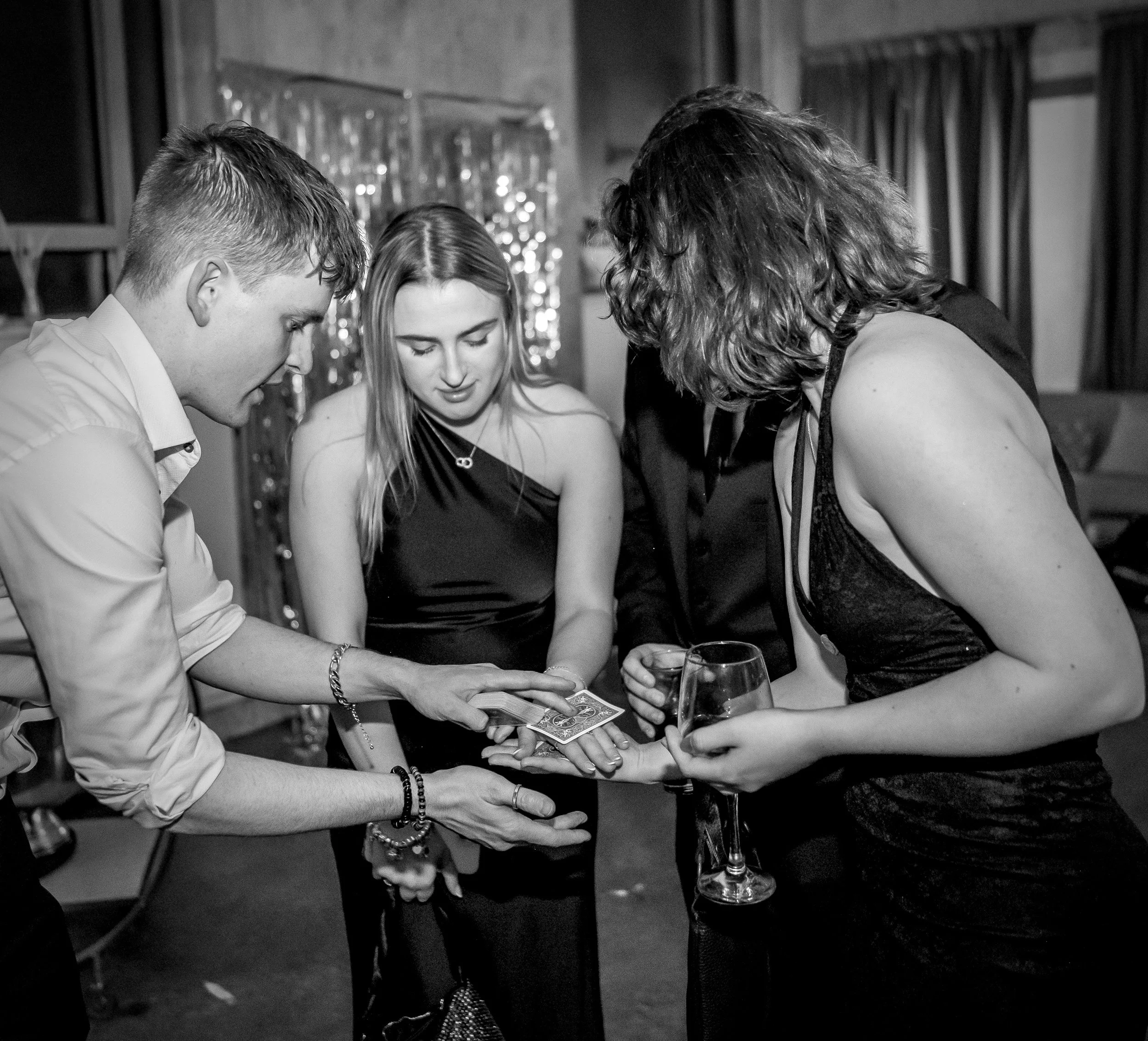 Group of guests watching a magic trick with cards at a party. They are focussed on the amazing magic trick performed in their own hands. 