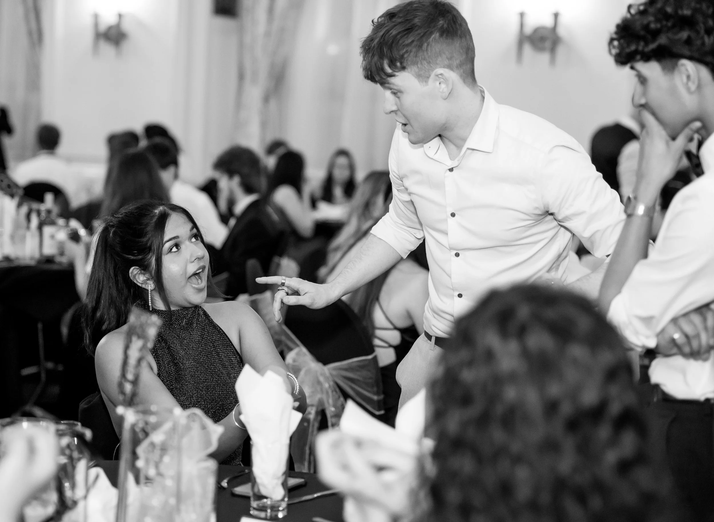 Group of people at a formal event, one woman with an amused expression, engaged in conversation with two men watching Manchester Wedding magician Daniel Maze. 