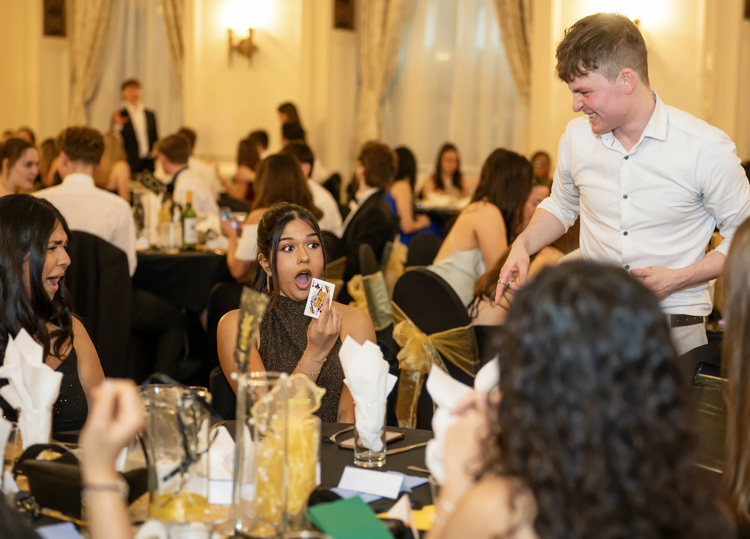 People at a formal event reacting to a card magic trick performed by Daniel Maze, Manchester magician.