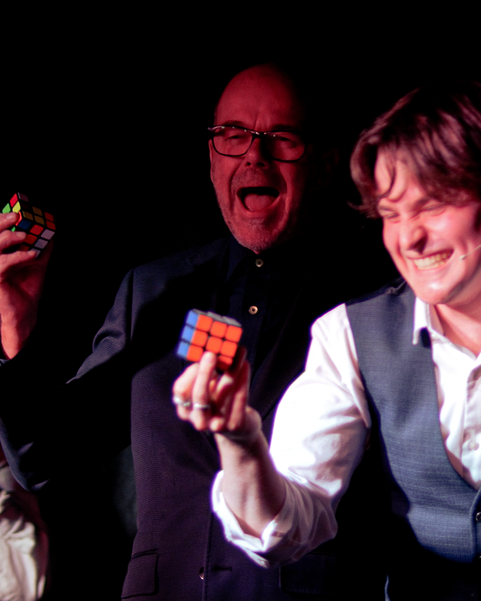 A group of people at a party, with one woman looking surprised and holding a bottle. Another person, wearing white, holds a glass. The setting appears lively, suggesting social interaction and celebration. Reacting to unforgettable magic. 