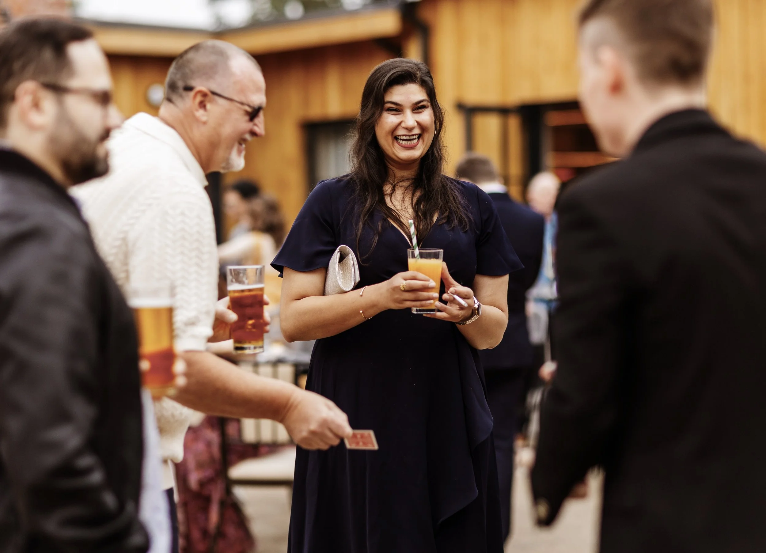 Group of people laughing and holding drinks at a social gathering outdoors at a Wedding with Daniel Maze. 