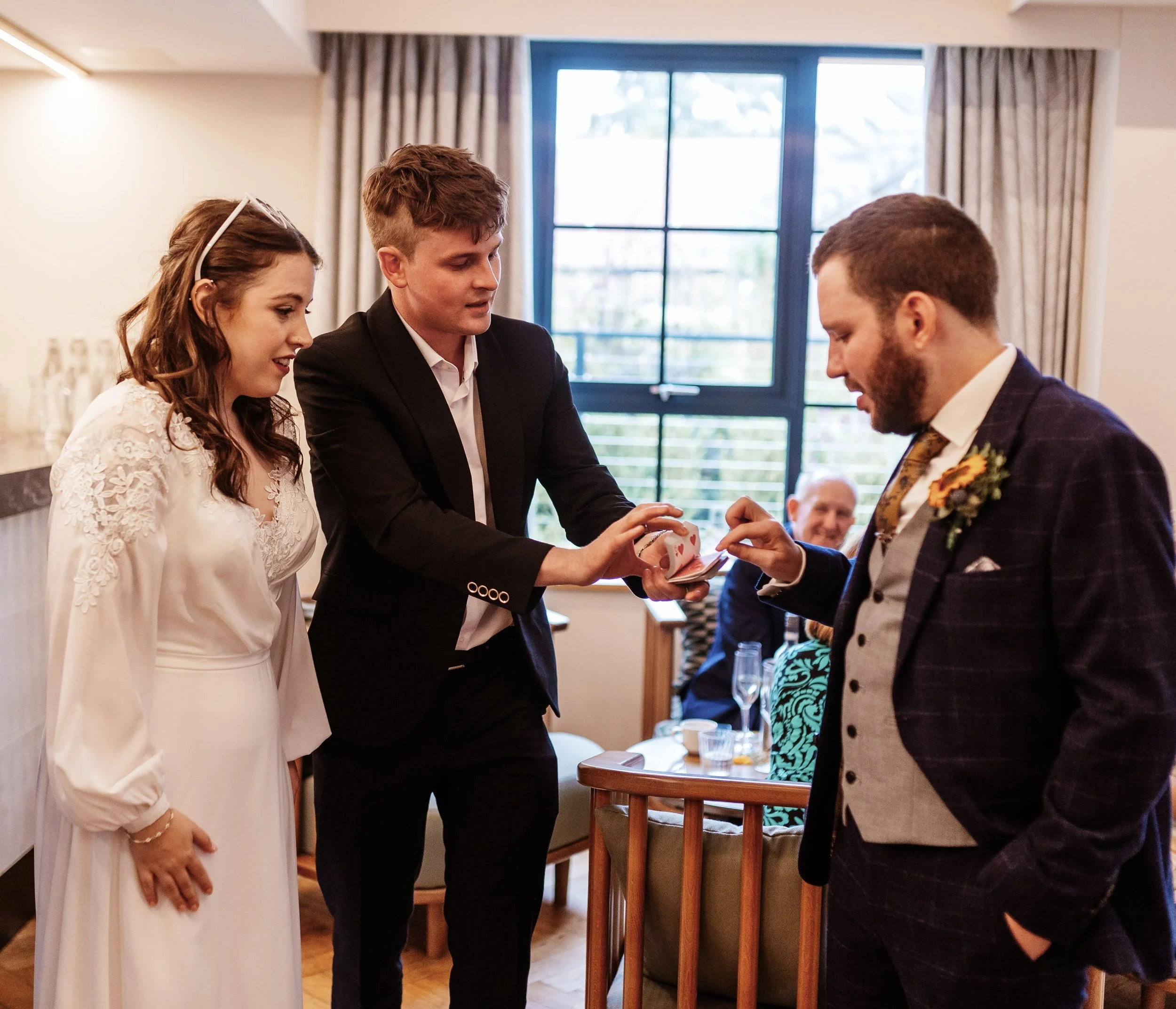 A wedding guest performing a card trick for a bride and groom indoors. Magic reaction to unforgettable entertainment. 