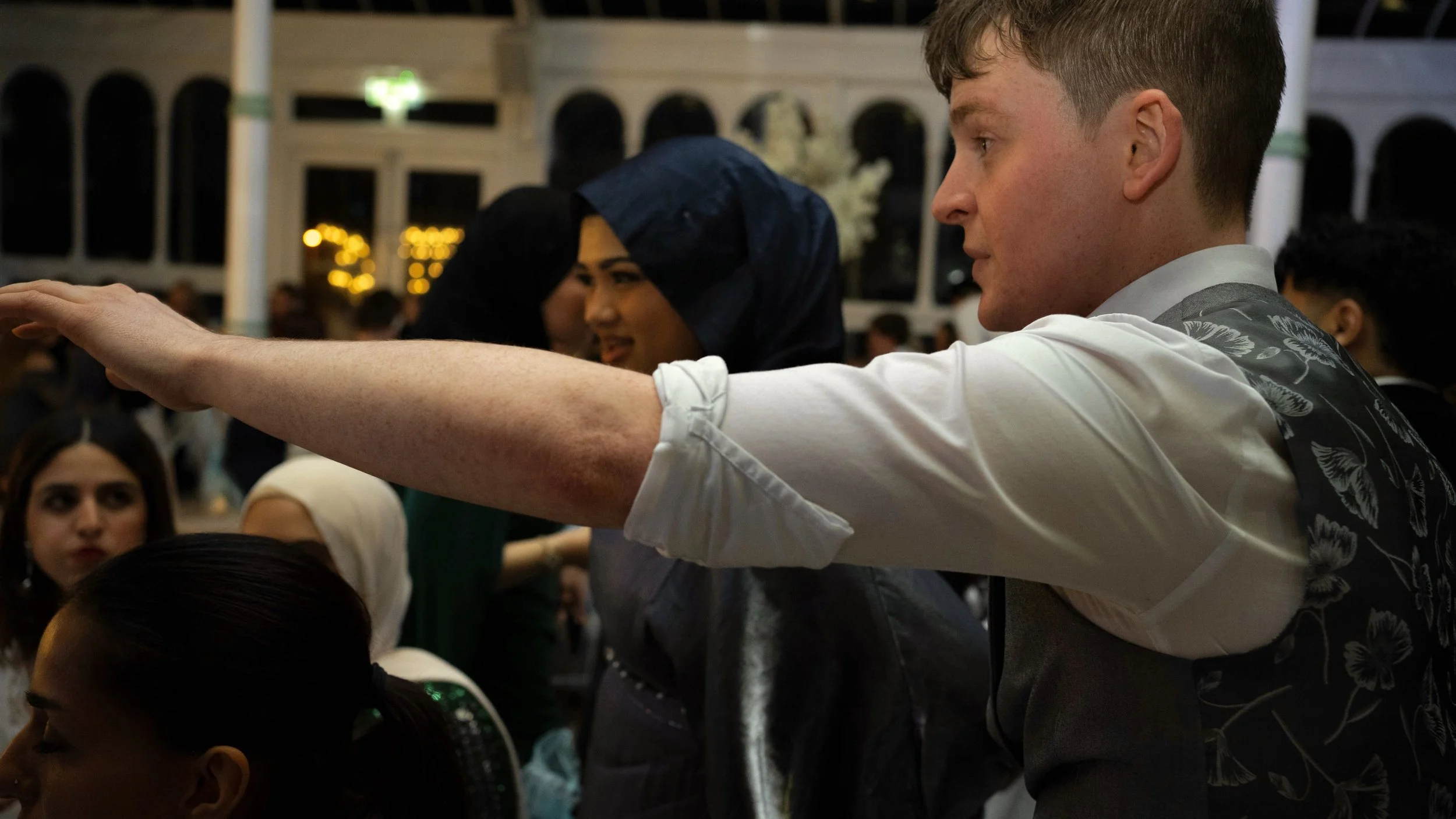 People dressed formally at a social event, with a Daniel Maze the magician extending his arm and other attendees engaged in conversation.