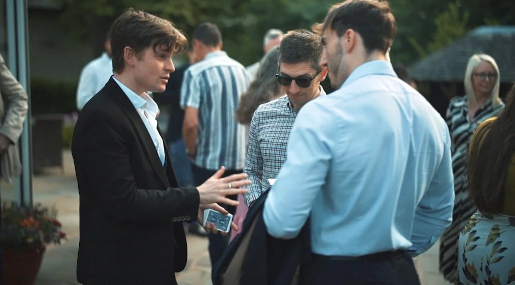 Three men engaged in a conversation at an outdoor event, with other people in the background. Daniel Maze performing mentalism. 