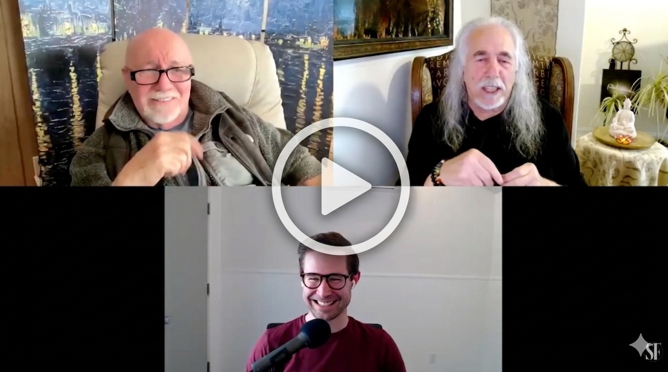 Three men participating in a video call, two in a split-screen frame at the top and one at the bottom. The man on the top left wears glasses and a brown jacket, the man on the top right has long gray hair and a beard, and the man on the bottom has short dark hair, glasses, and a red shirt, smiling with a microphone in front of him.