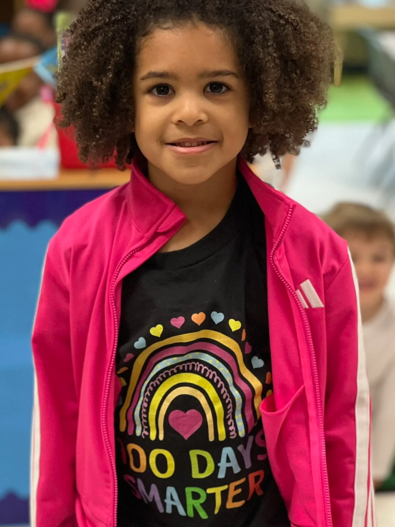 A girl wearing a pink jacket and smiling.