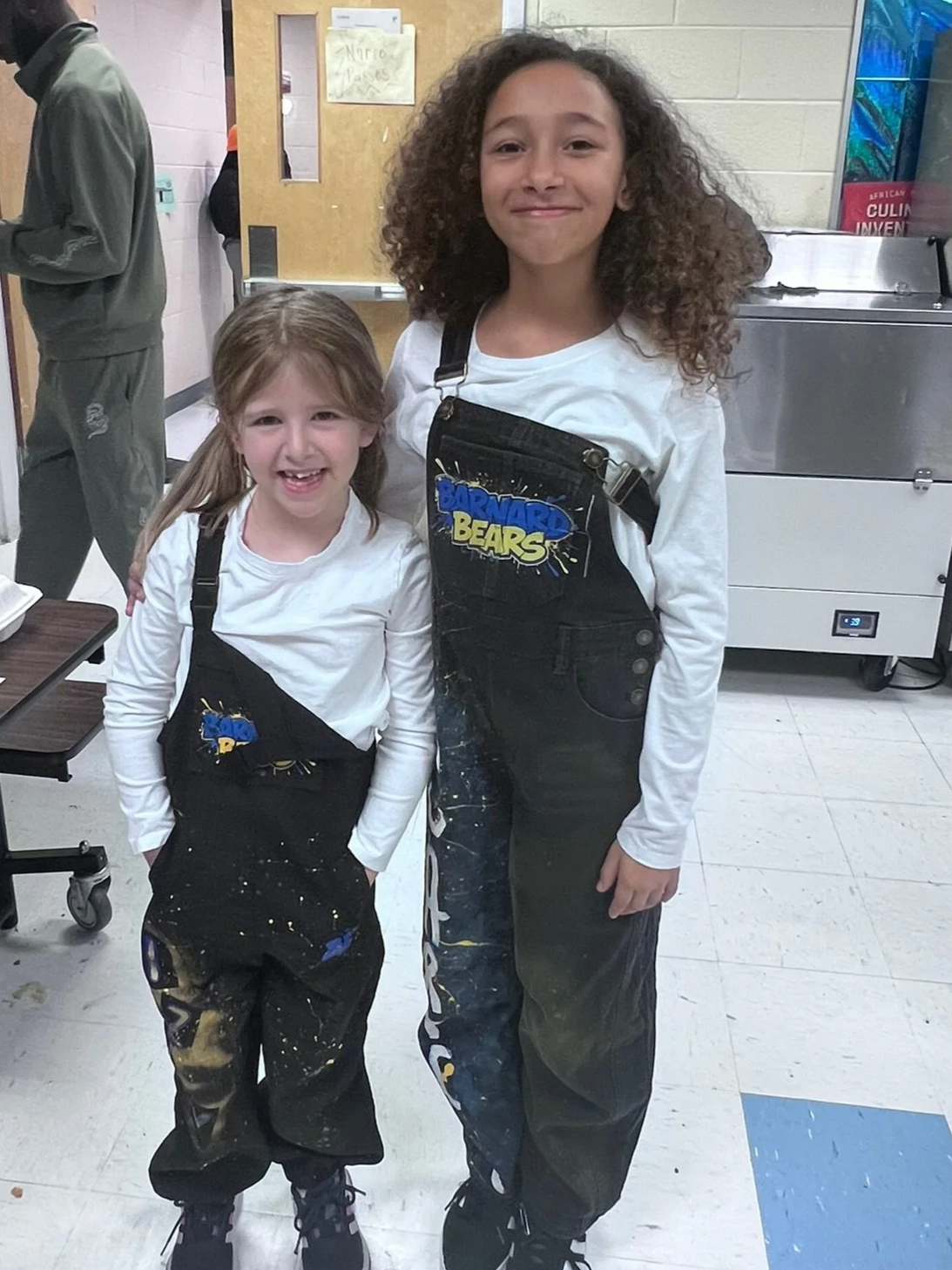 Two students wearing matching Barnard overalls; smiling at the camera.