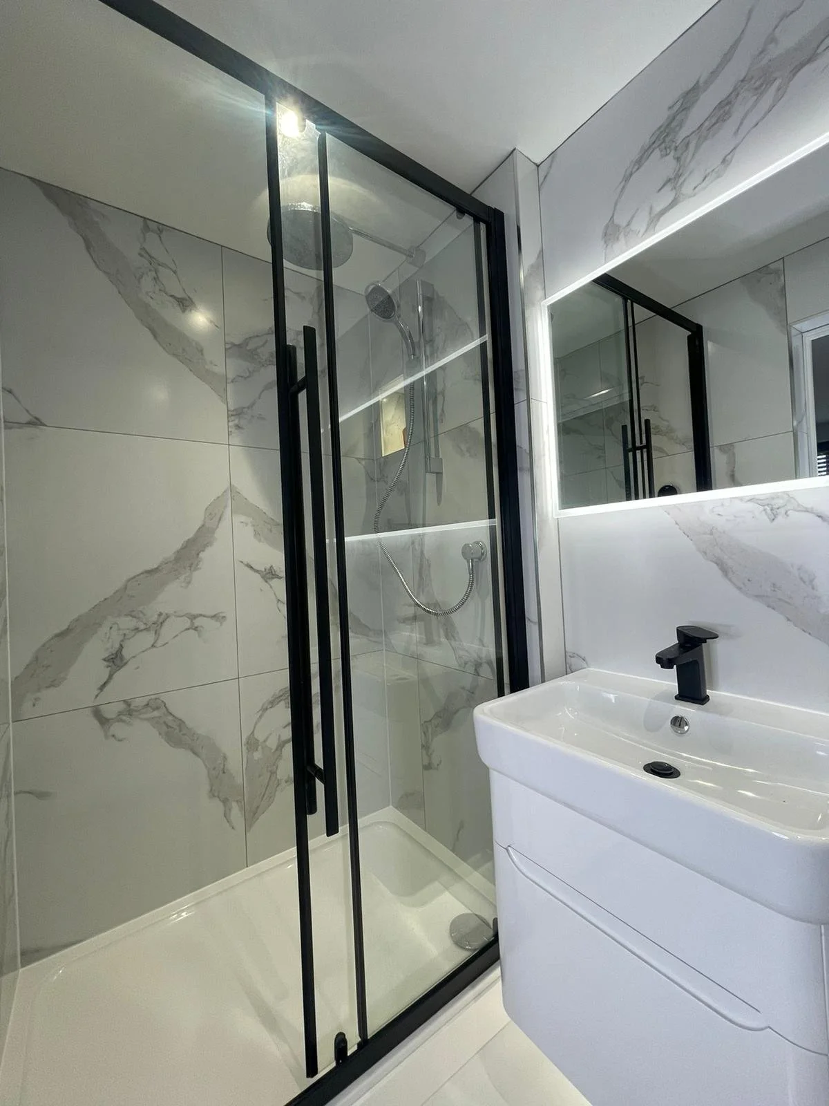 Modern bathroom with glass shower, marble tiles, white sink, and black fixtures.