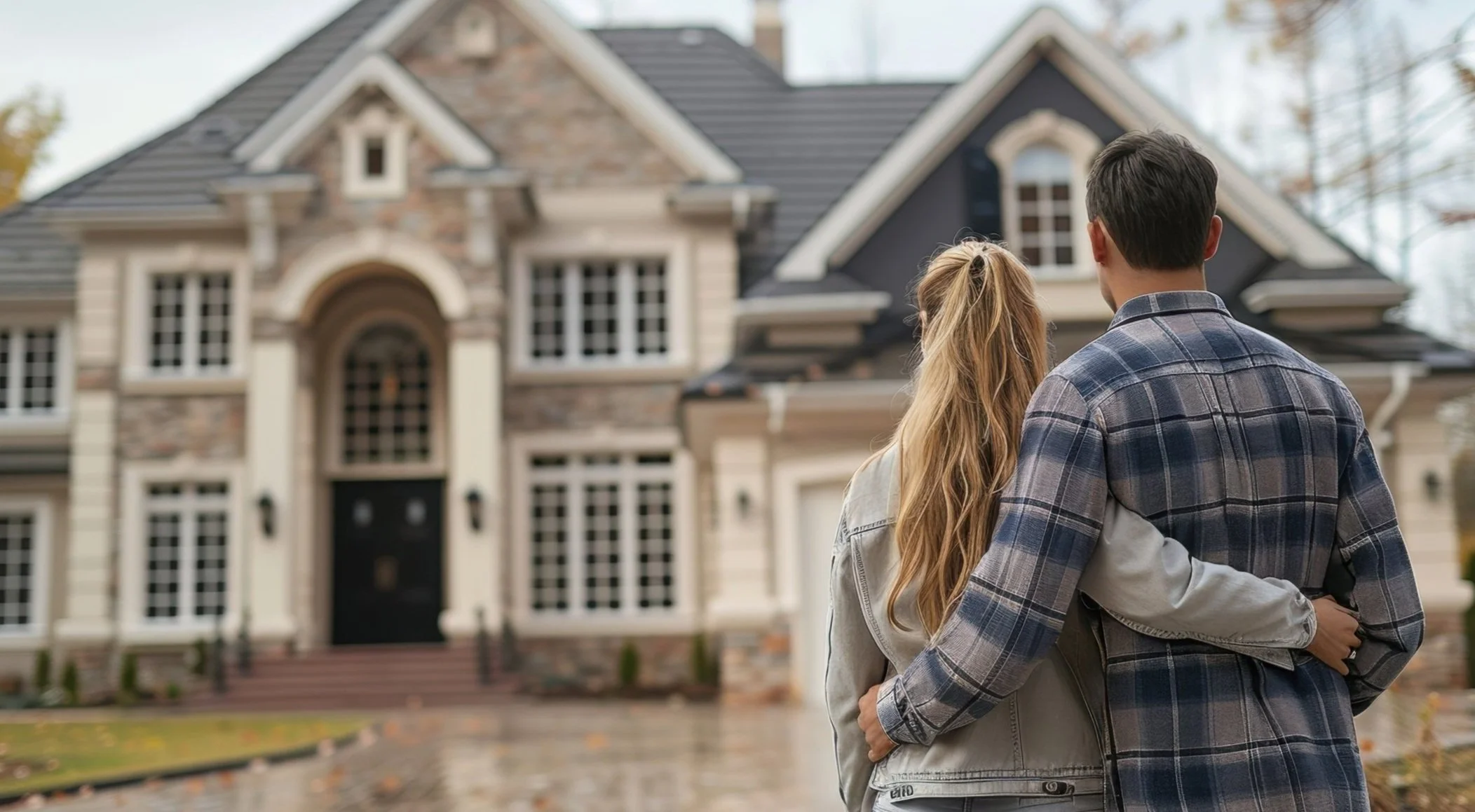 A couple standing arm-in-arm facing a large, elegant house.