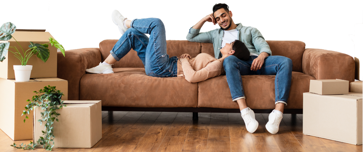A couple relaxing together on a leather couch in their new home, surrounded by moving boxes and plants