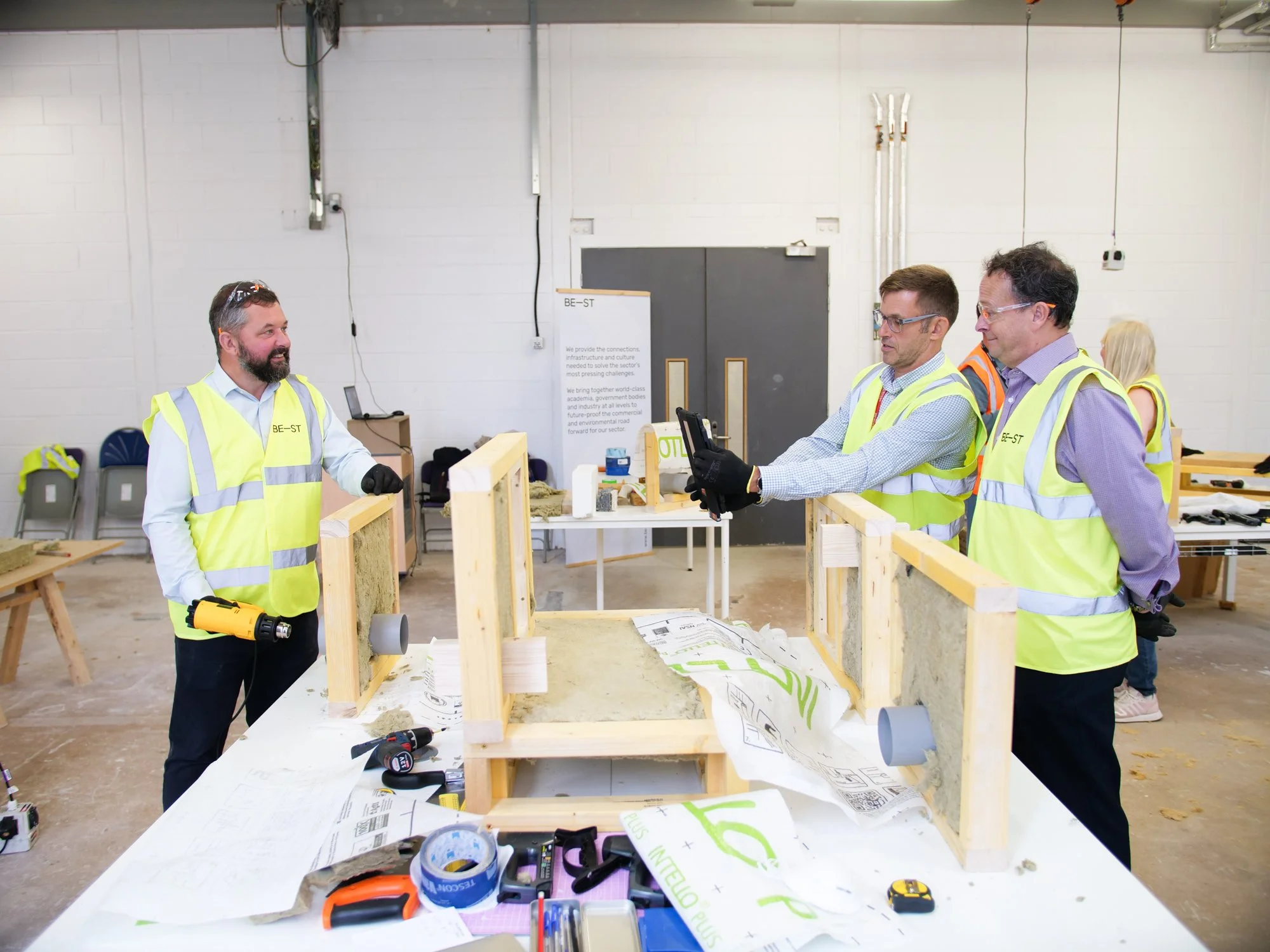 Three men wearing high vis vests, working over over a work station with planks of wood. One man is using an a device to check wood.