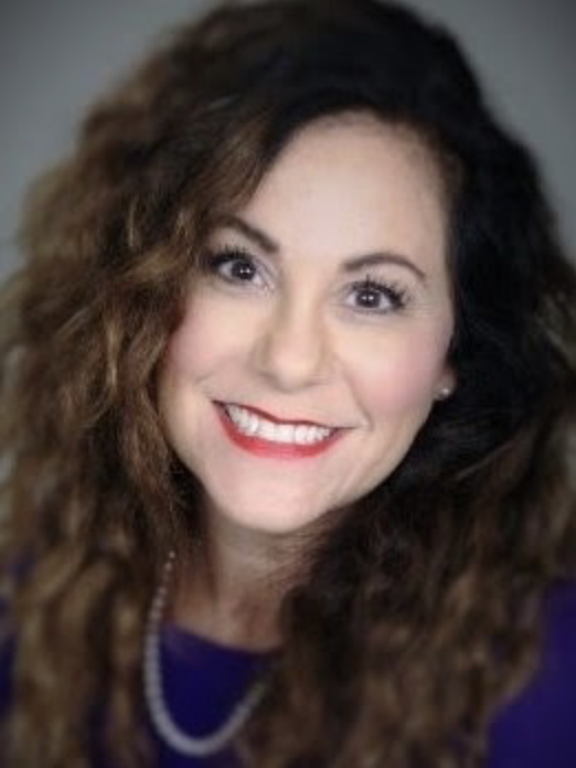 A woman with curly brown hair, wearing a pearl necklace and a purple top, smiling at the camera.