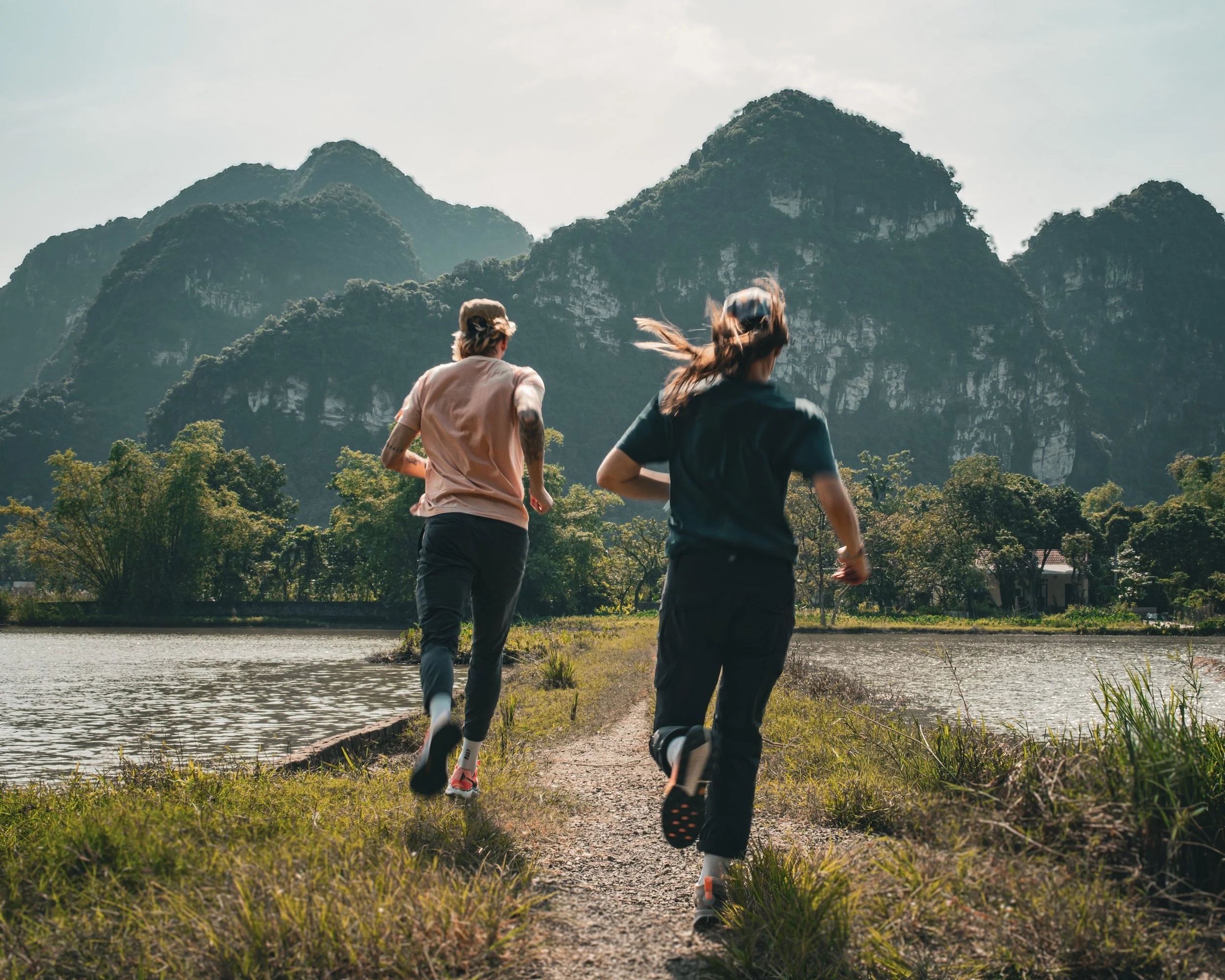 Founders of Lost Wolves Creative running along a lakeside trail in Vietnam with lush green mountains in the background