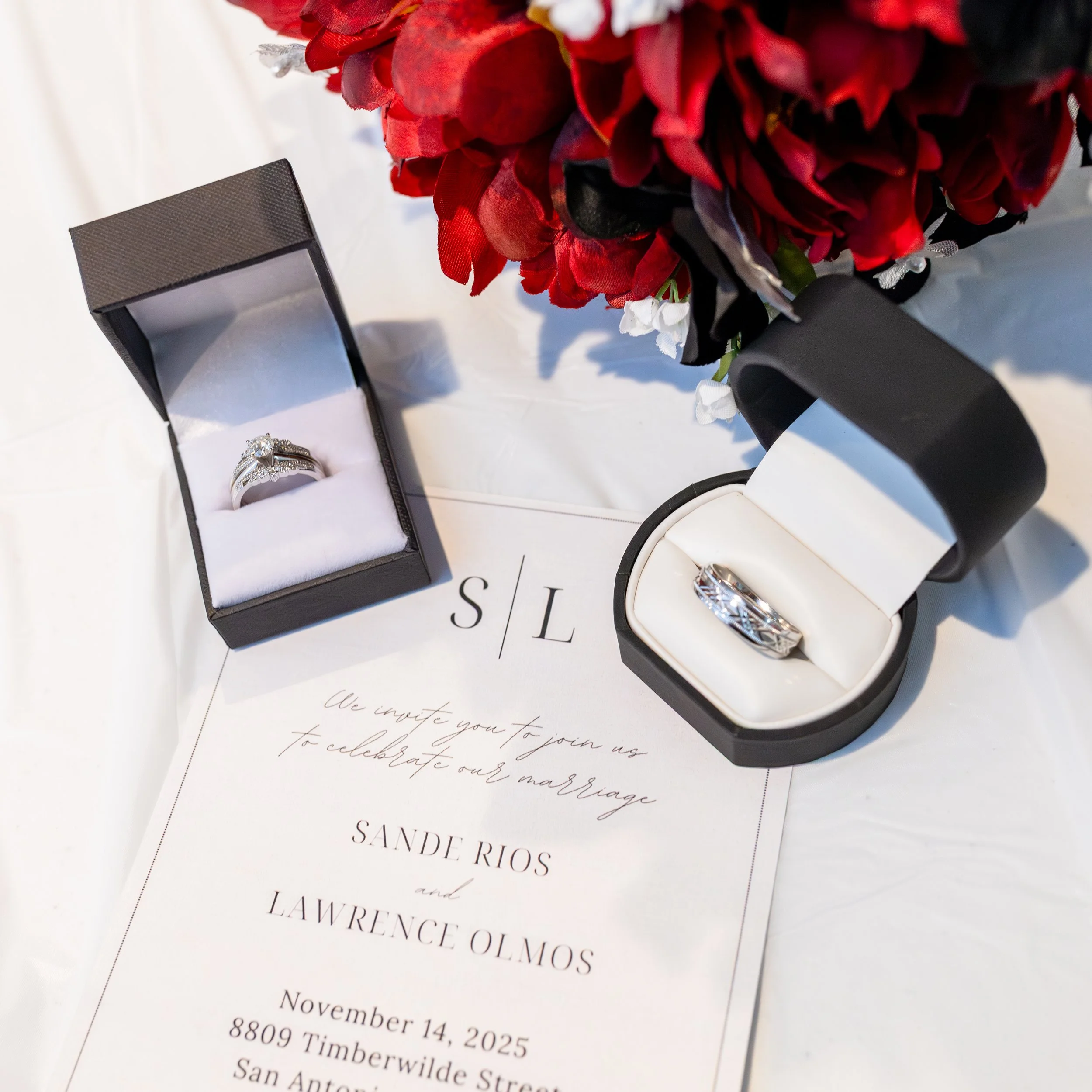 Wedding invitation with two rings in black and white boxes, red floral arrangement.