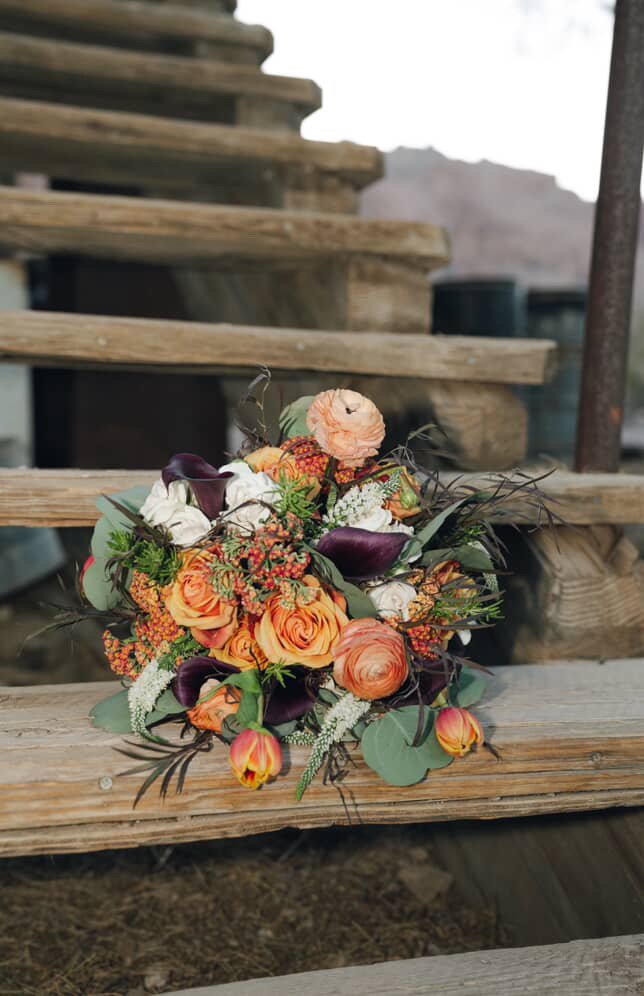 A bouquet of various flowers including roses, calla lilies, and tulips resting on wooden steps outdoors.