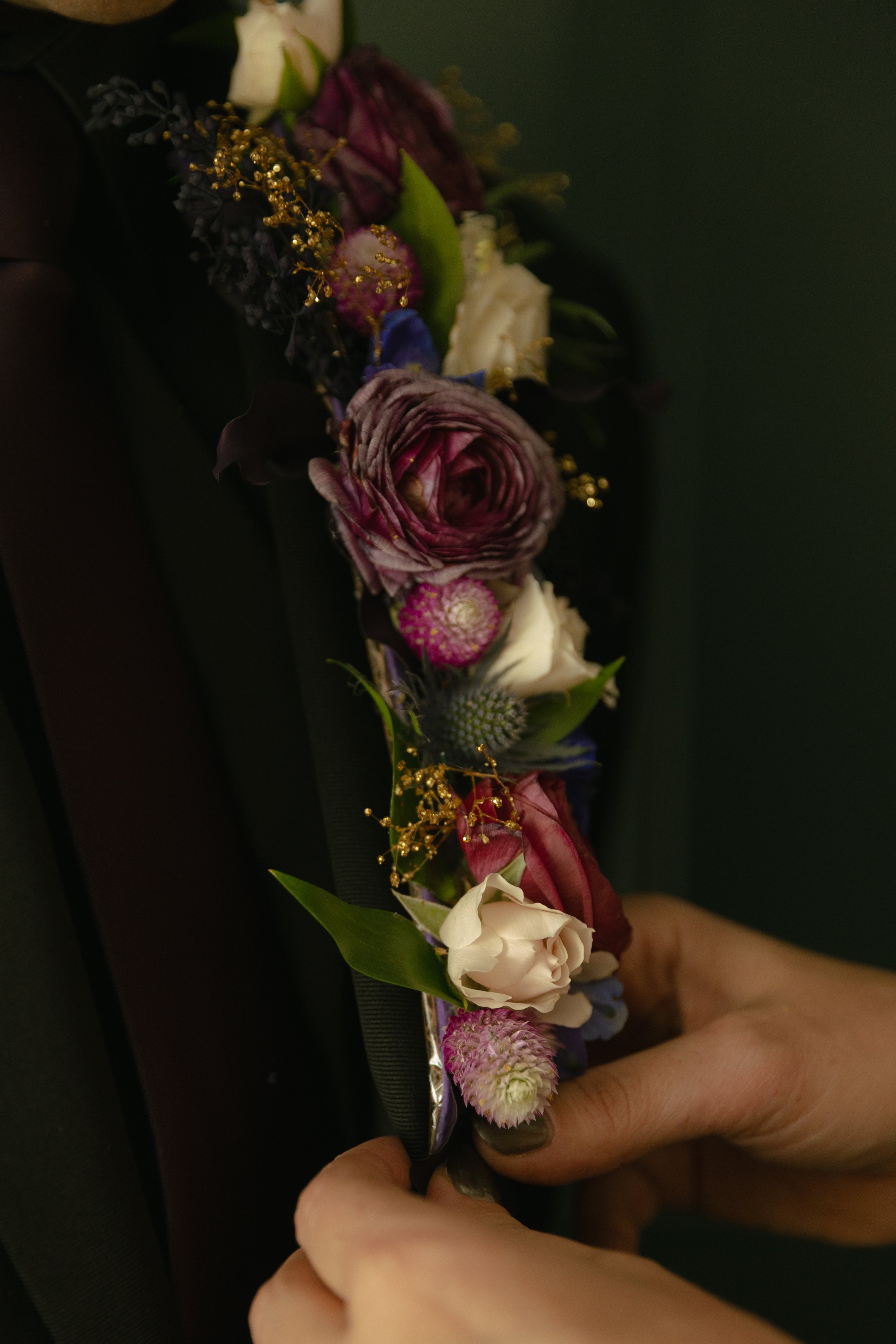 Close-up of a floral corsage with various colored flowers and greenery held by a person's hand.