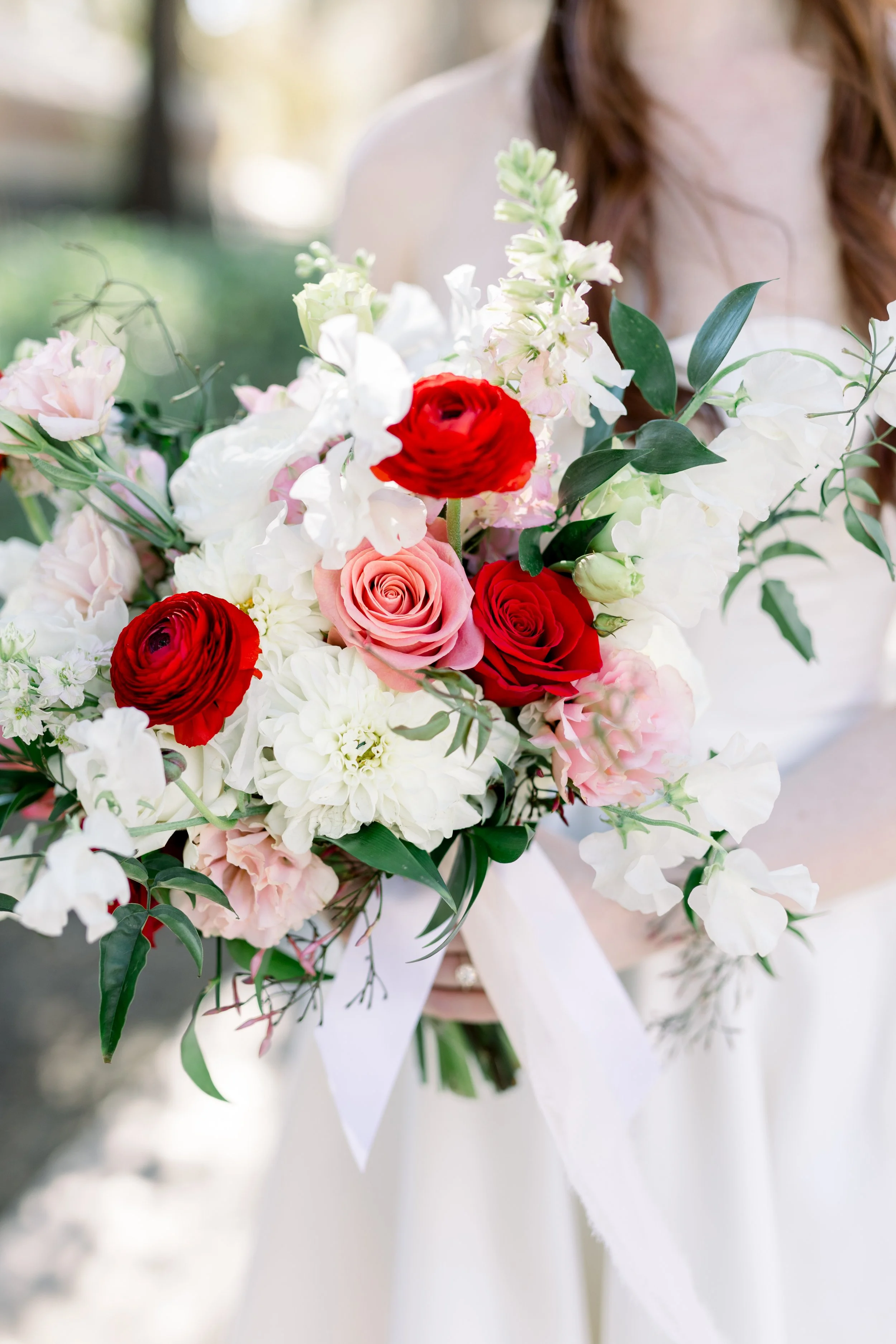 A bride holding a colorful bouquet of roses, ranunculus, sweet peas, and greenery.