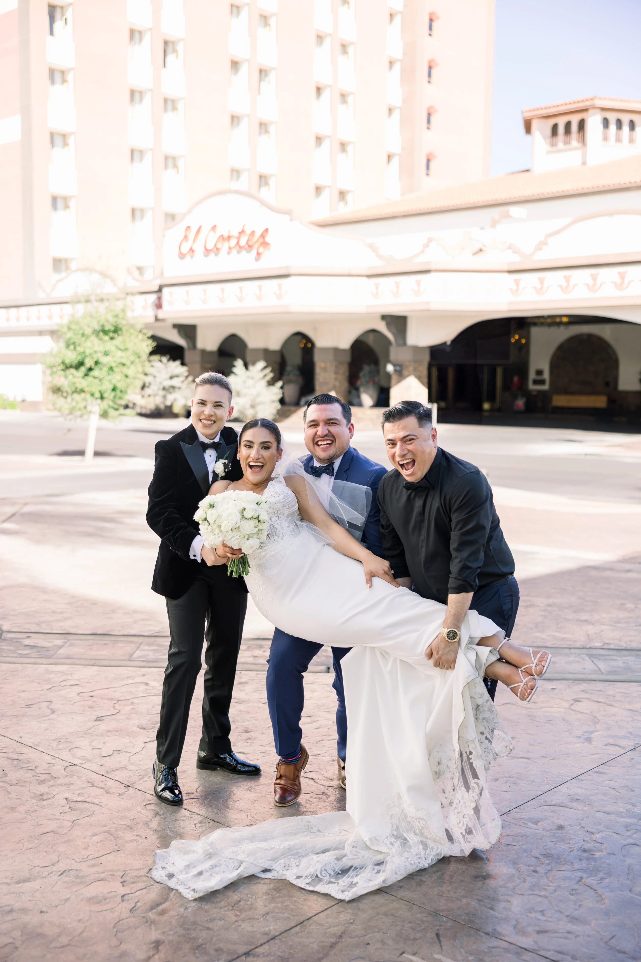 A bride being carried by three groomsmen outside of a hotel named El Cortez.