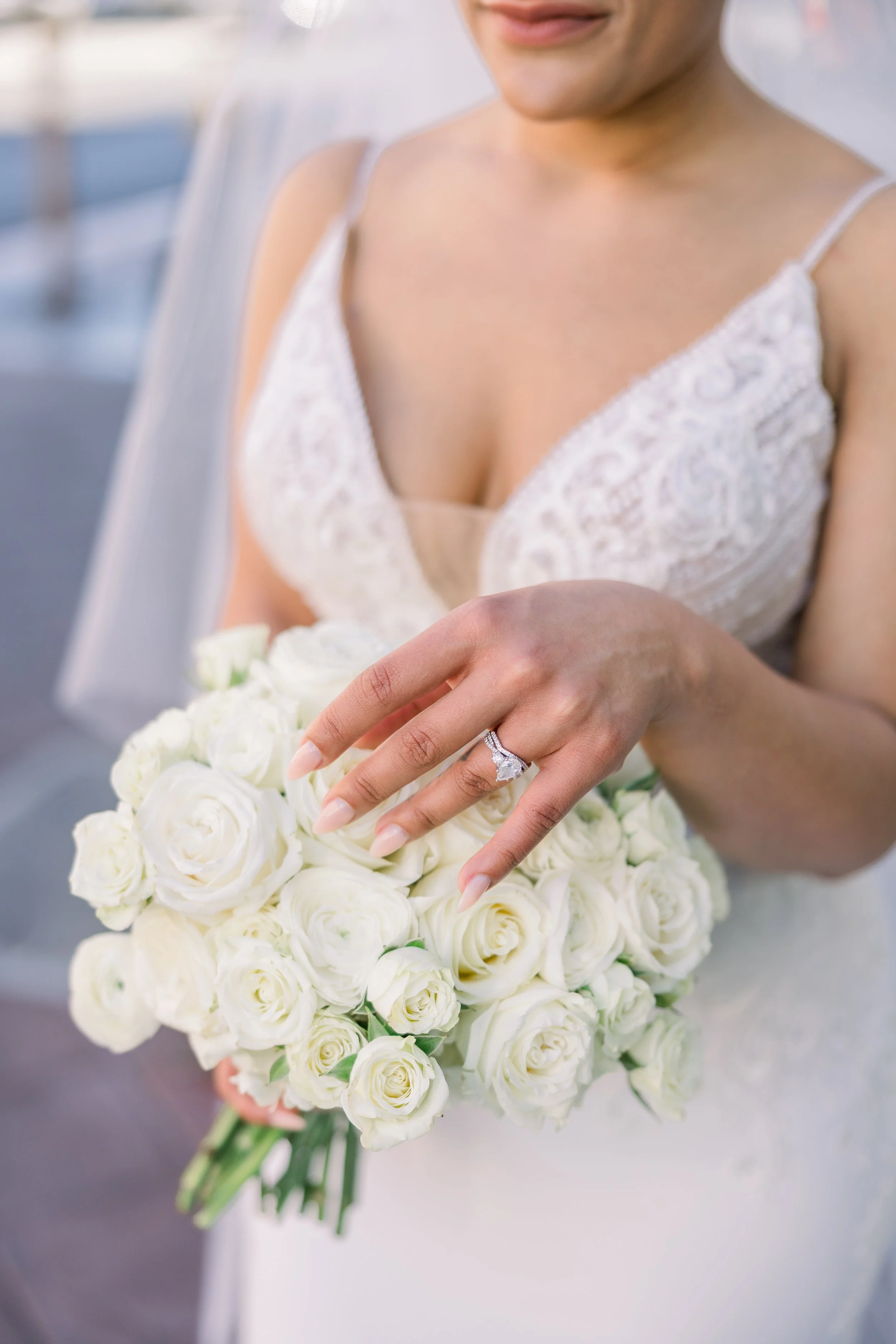A bride displaying her engagement ring on her left hand while holding a bouquet of white roses.