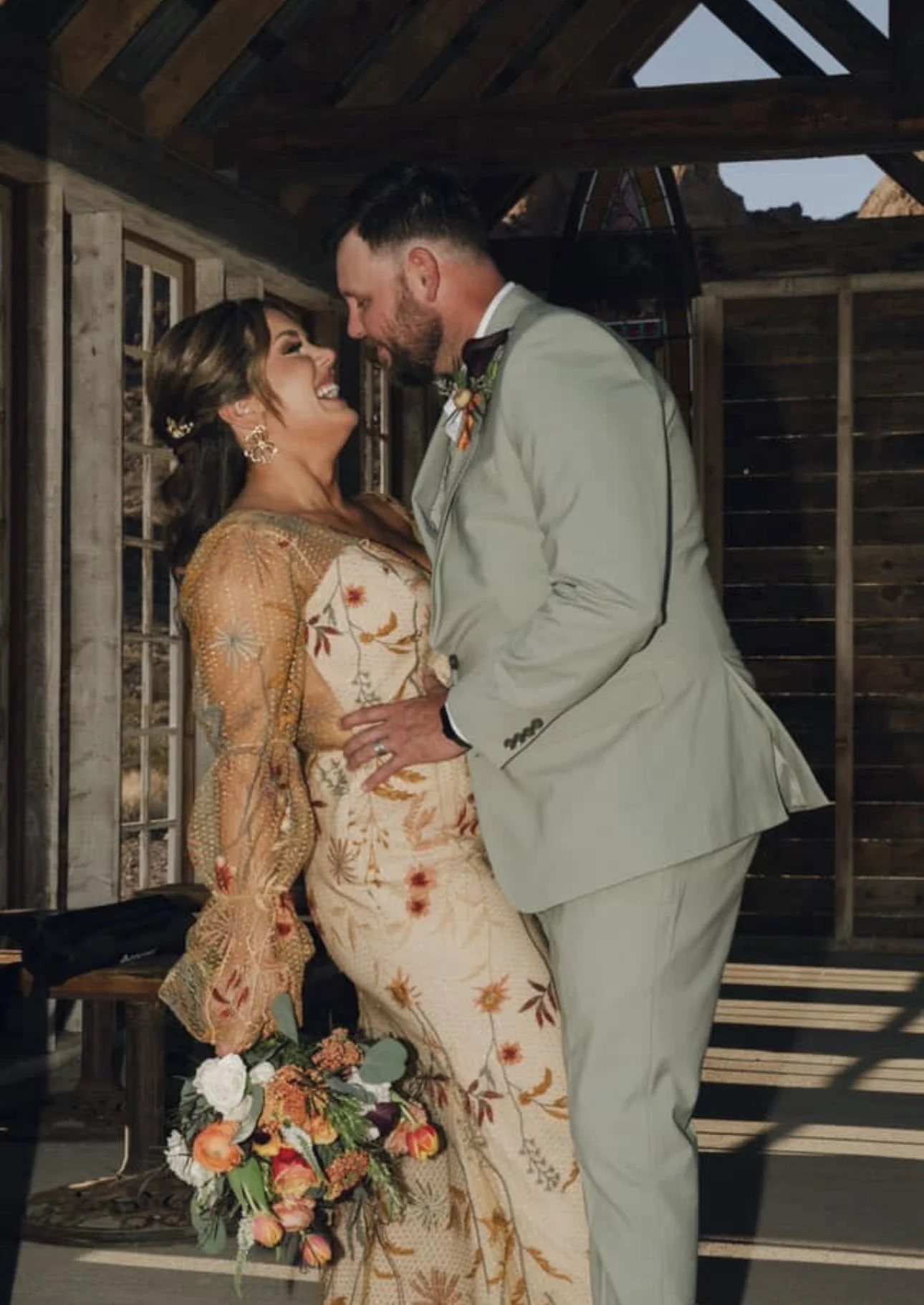 A couple dressed in wedding attire sharing a joyful moment indoors, with the woman holding a bouquet of flowers.