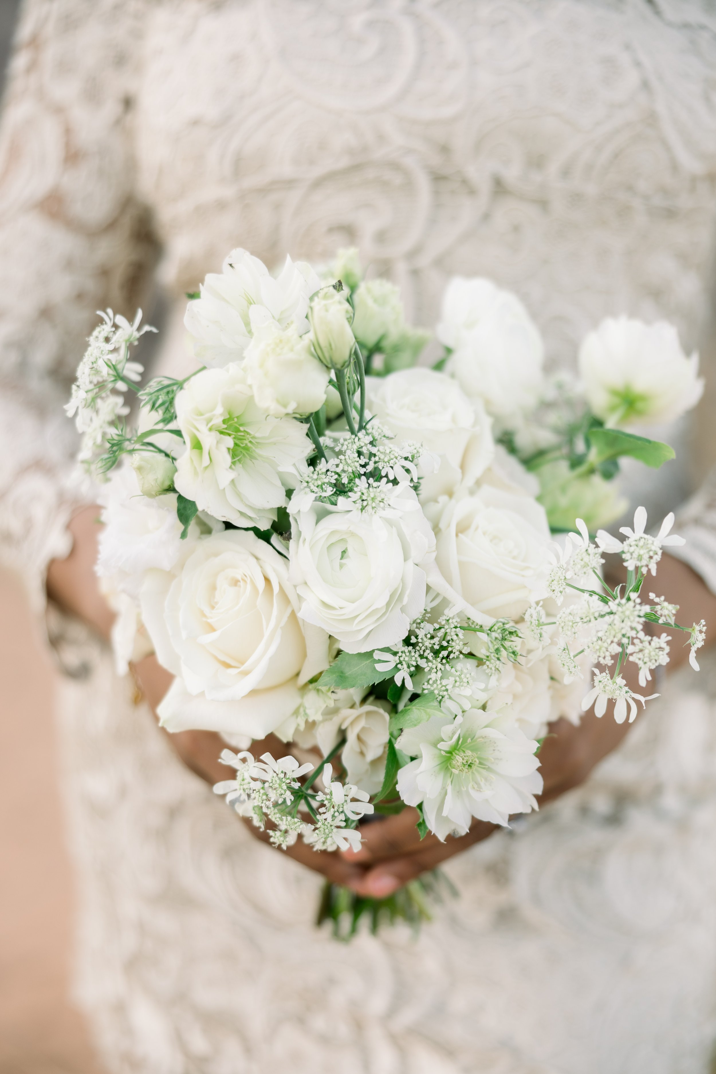 A person holding a bouquet of white flowers including roses, ranunculus, and other delicate blooms.