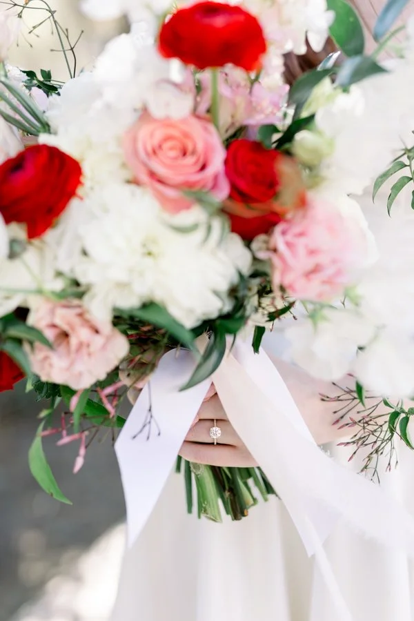 Person holding a colorful bouquet of flowers, showing a wedding ring on their finger.
