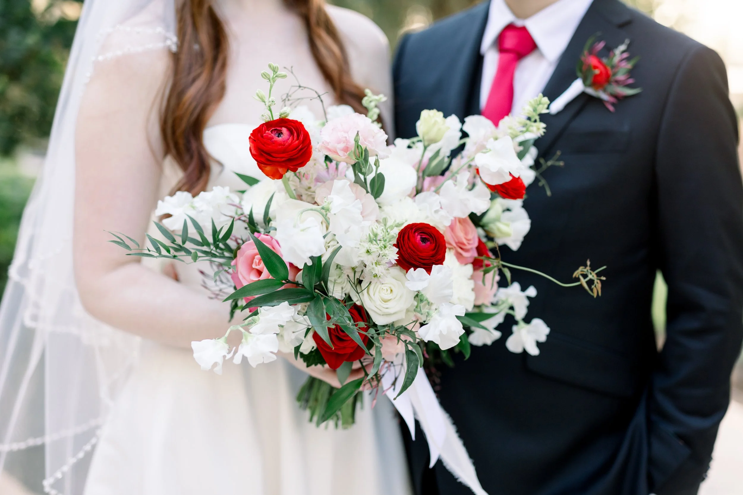 A bride and groom holding a large bouquet of pink, white, and red flowers during their wedding.