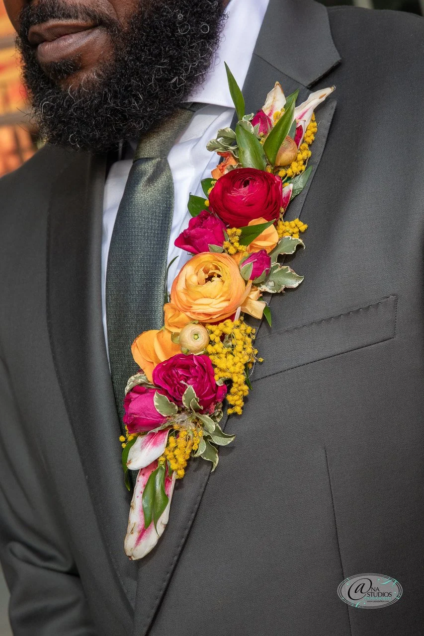 Close-up of a man in a black suit and tie wearing a colorful flower boutonniere on his lapel.