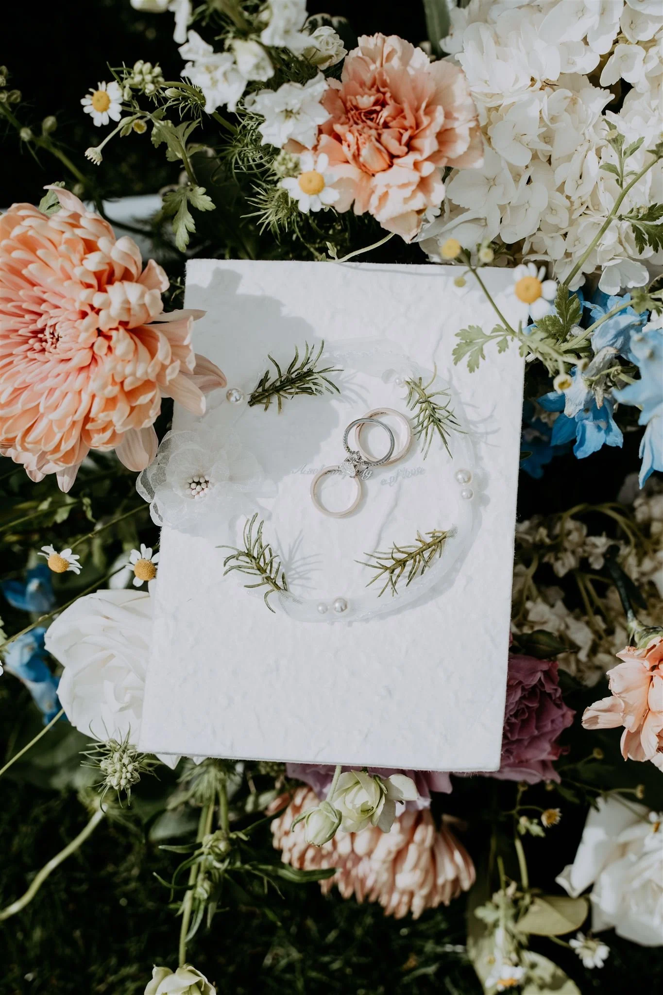 Wedding rings on a white card surrounded by flowers and small decorative items.