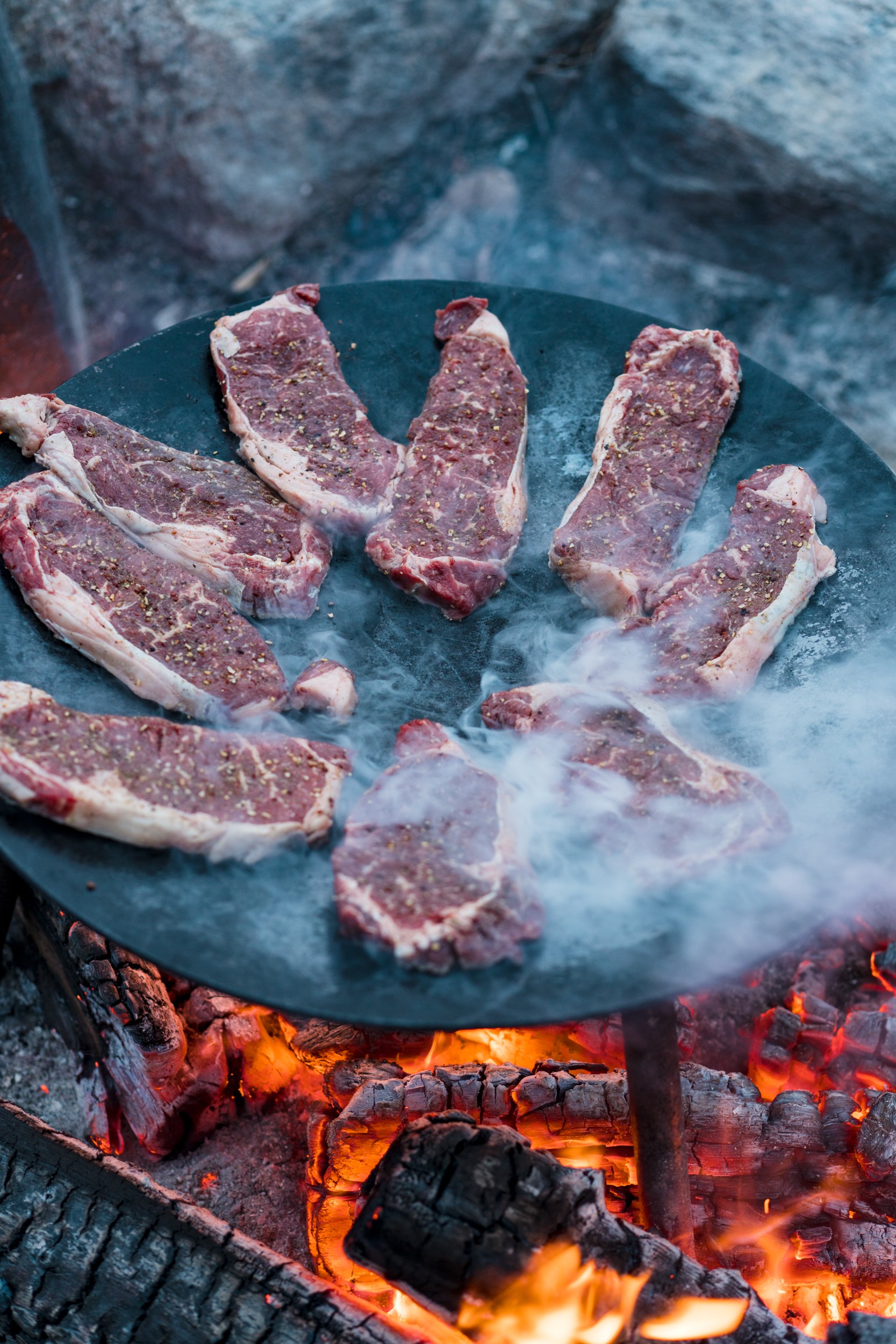 Raw beef steaks seasoned with spices cooking on a hot grill over an open flame.