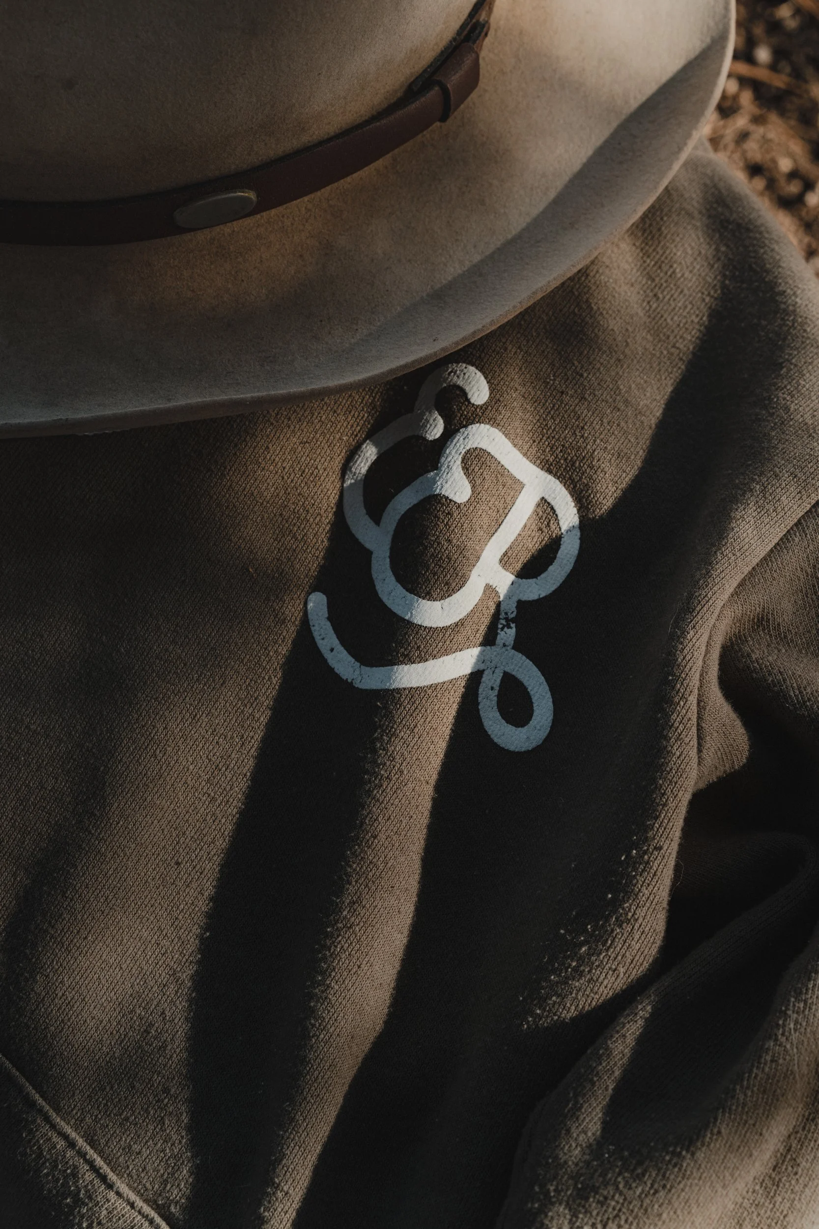 Close-up of a brown jacket with a white stethoscope logo and a beige fedora hat resting on it.