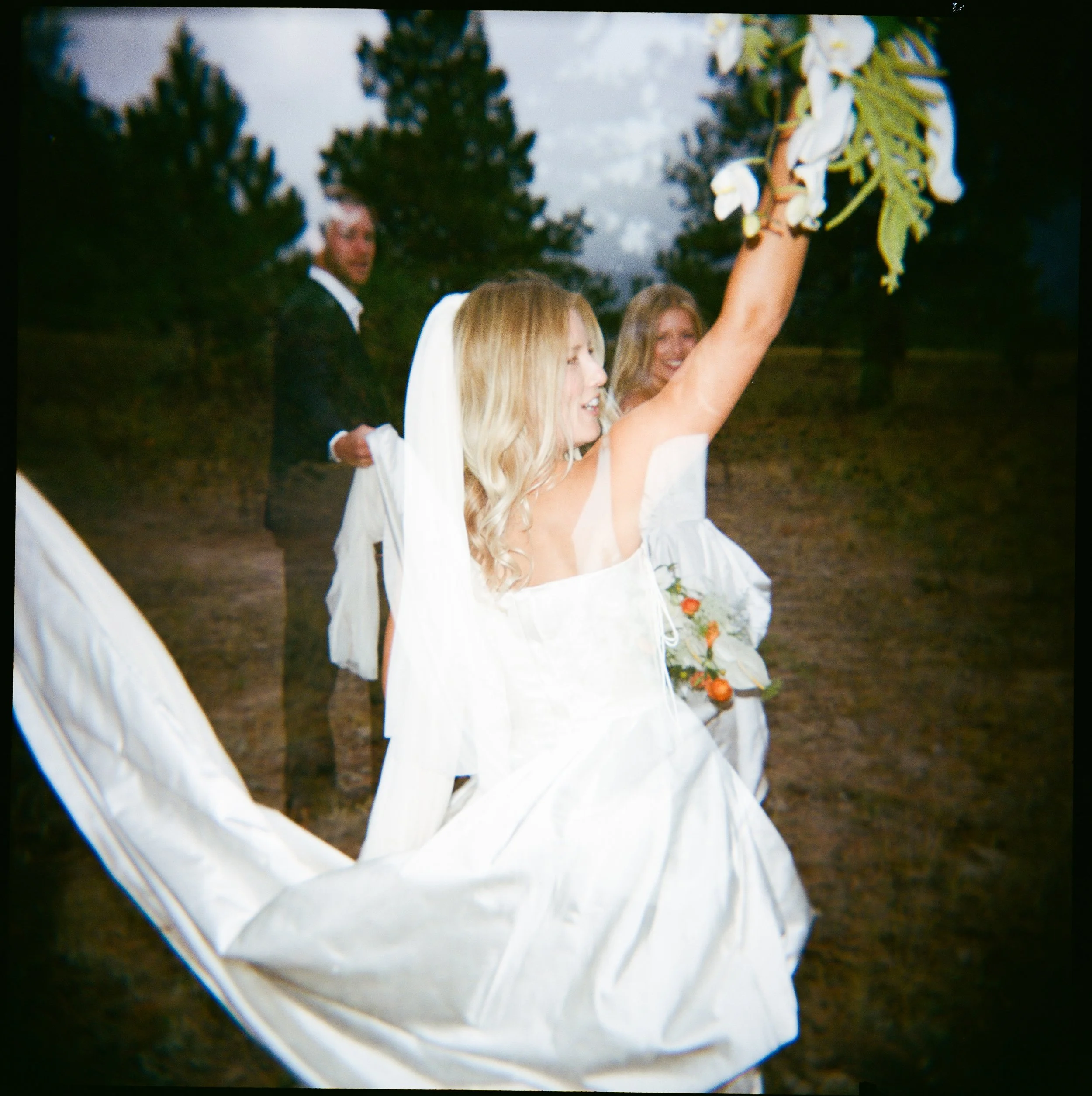 Bride in a white wedding dress and veil, holding a bouquet, outdoors with trees, celebrating at her wedding.