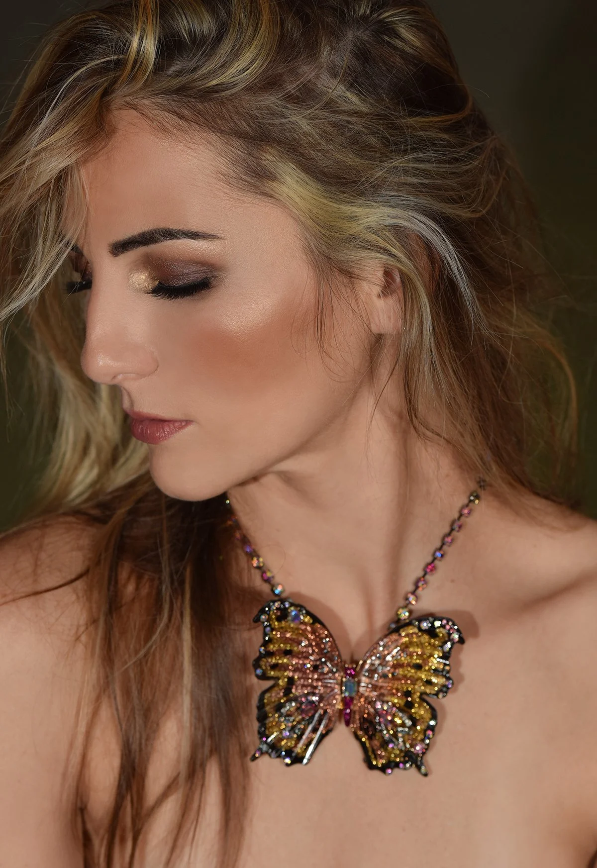 Close-up of a woman's face with makeup and long hair, wearing a butterfly-shaped necklace.