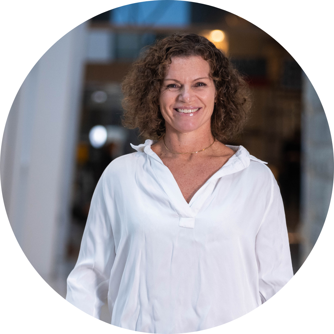 A woman with short, curly hair smiling in front of a textured wall and a sculpture.