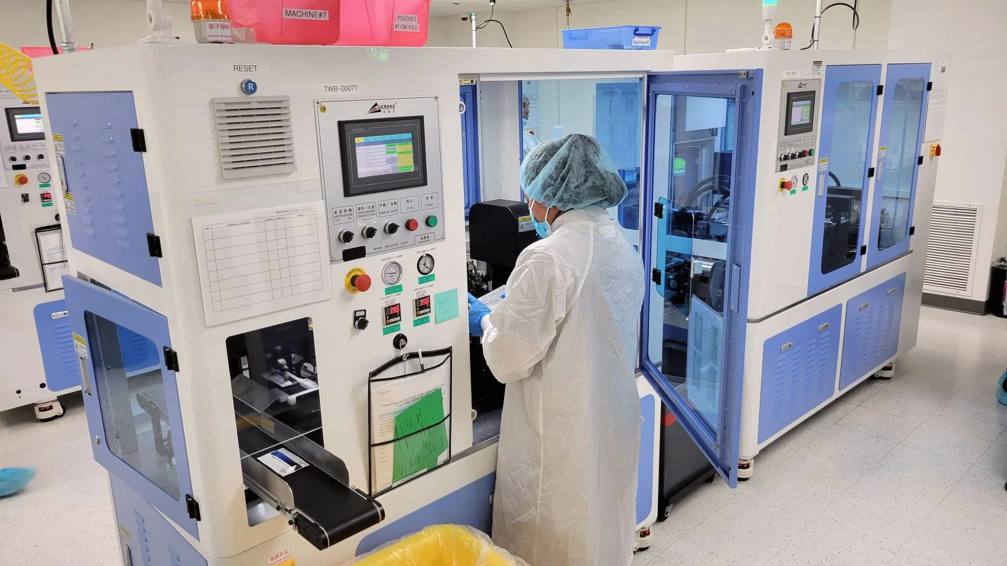 A lab worker wearing protective clothing, working with a large scientific instrument in a laboratory setting.
