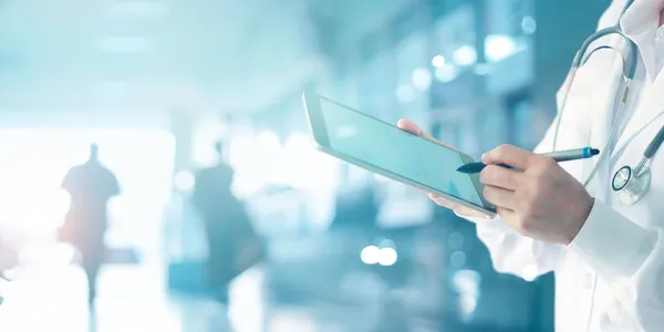 A healthcare professional holding a tablet with a stylus, in a medical setting.