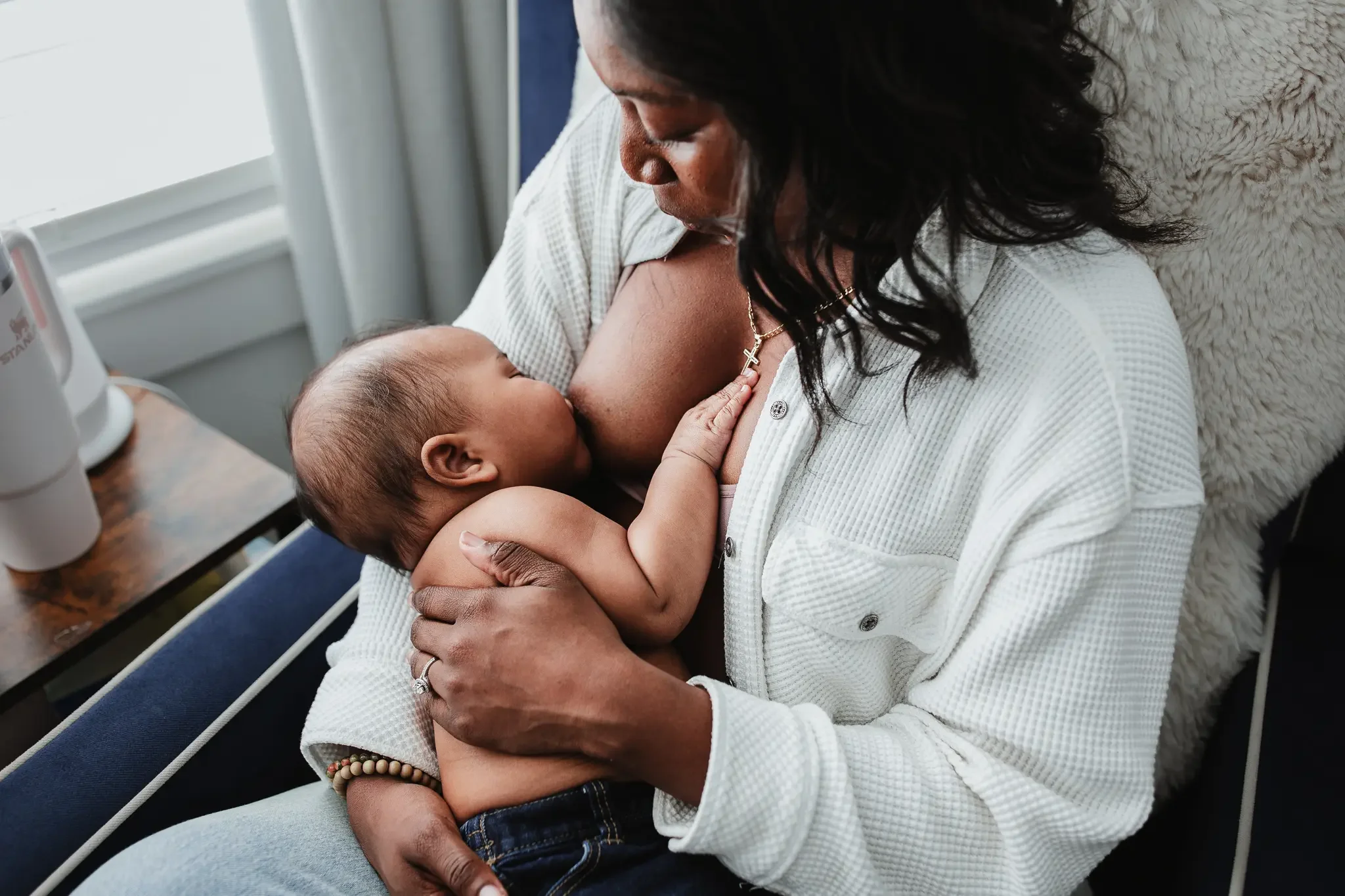 A black mother breastfeeds her baby boy in a rocking chair. Lifestyle in-home photography session by Brianna Trammell of The Nurturing Company.