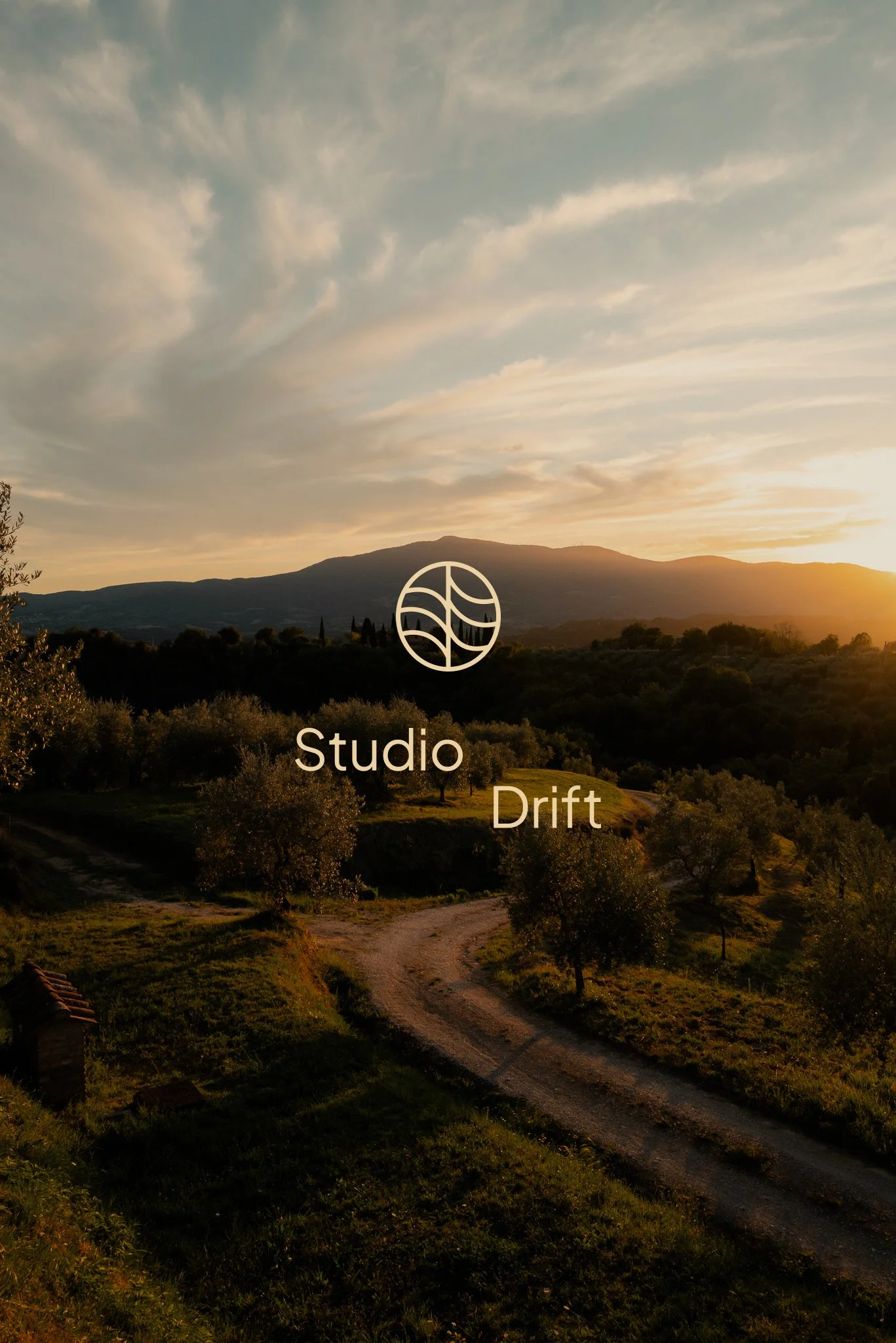 A scenic landscape of a dirt path winding through lush green trees with a mountain in the background during sunset or sunrise, under a sky with scattered clouds.