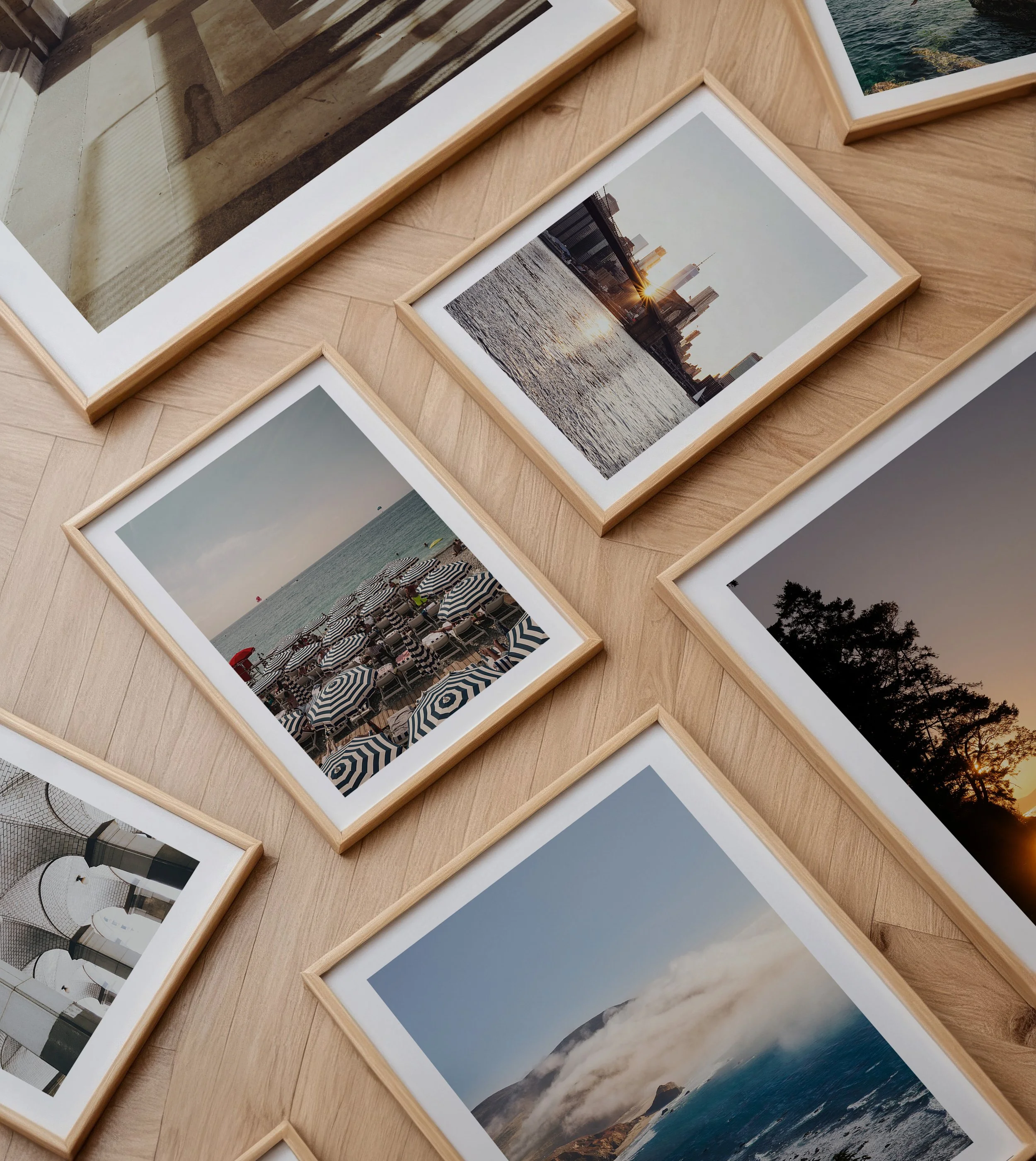 Set of framed photographs on a wooden surface, depicting a city skyline at sunset, a beach with umbrellas, and a foggy mountain scene.