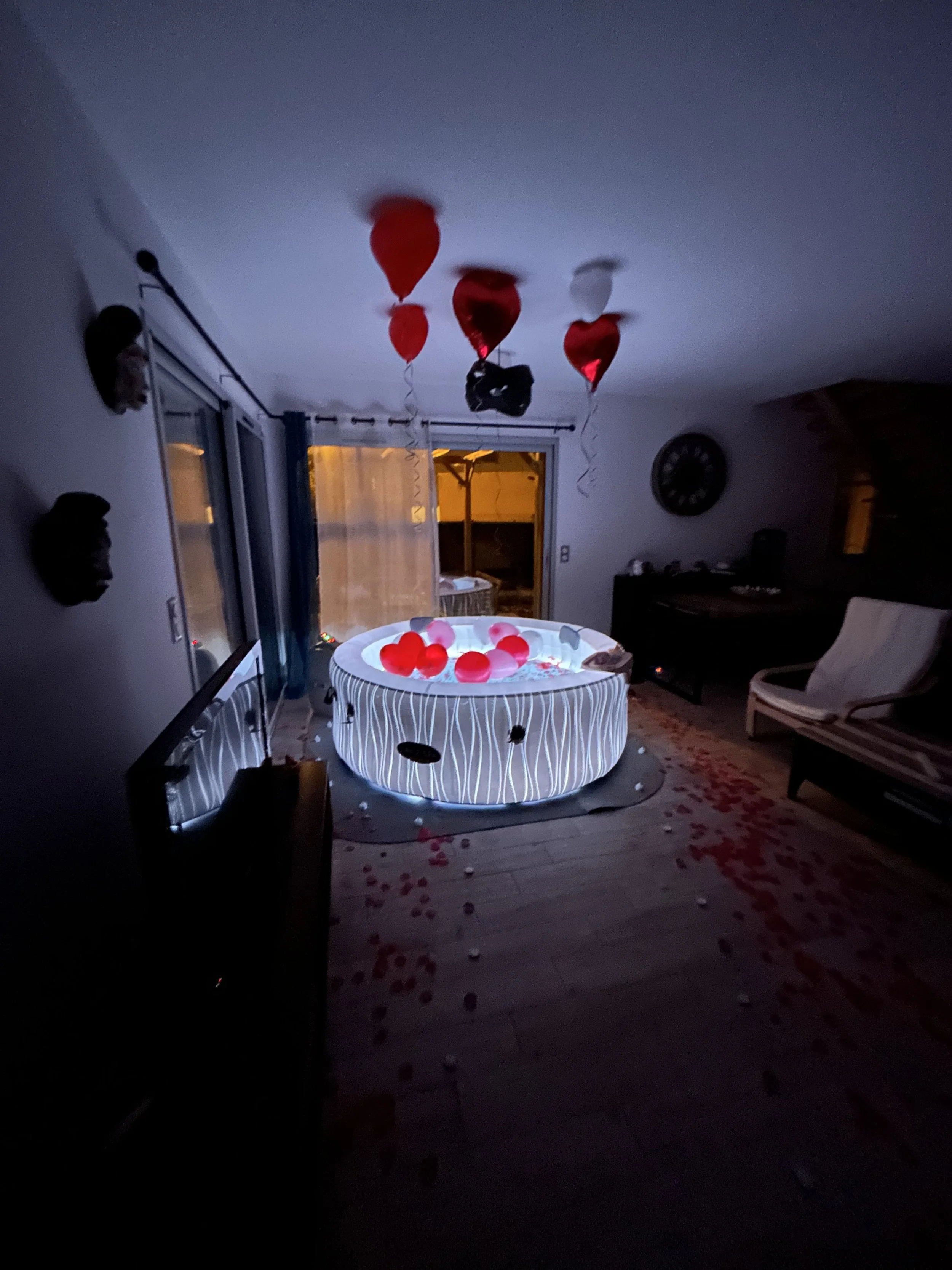 Un Jacuzzi intérieur décoré avec des ballons rouges et blancs, entouré de bougies et de pétales de rose, avec des lumières bleues à l'intérieur de la baignoire, dans une pièce à ambiance romantique.