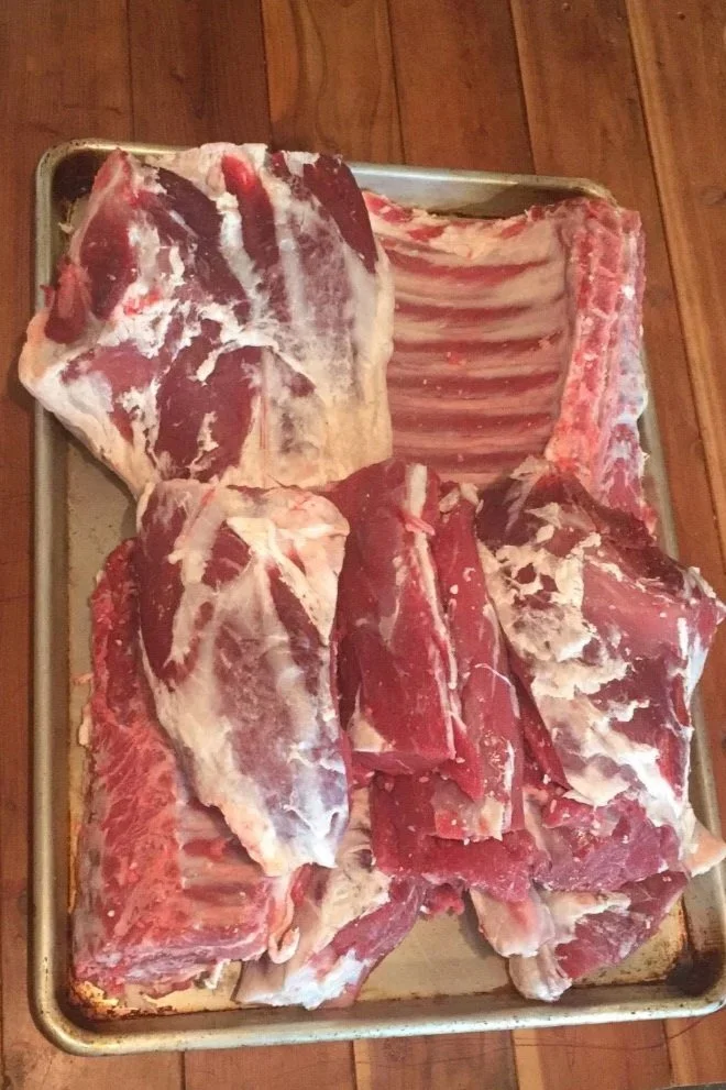 Various cuts of raw beef on a metal tray placed on a wooden surface.