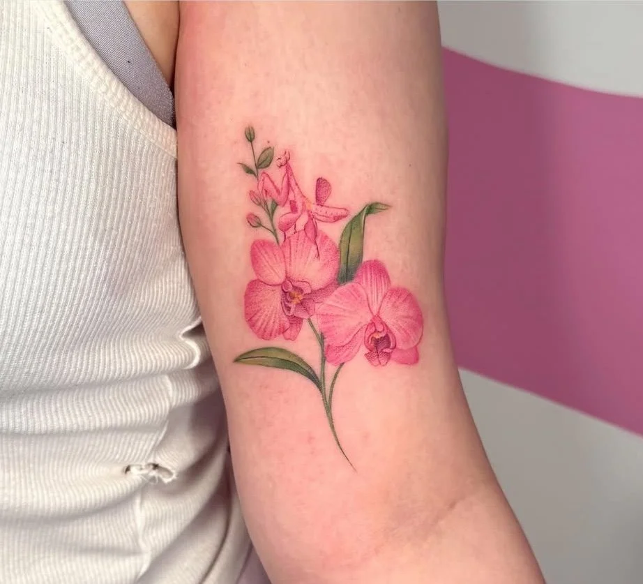 Delicate pink orchid tattoo with green leaves on the upper arm, in soft colour realism by guest artist Devin Evans