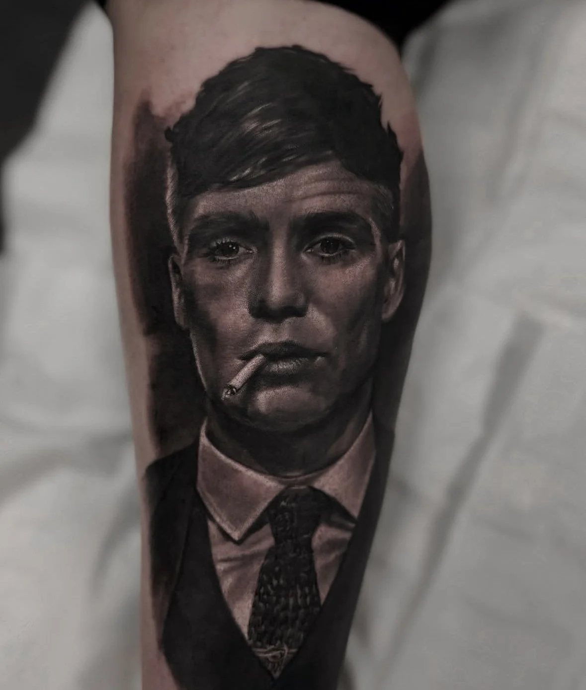Black and grey realistic portrait tattoo of Peaky Blinders character smoking cigarette by Andrei Cotici at FYNE Leeds