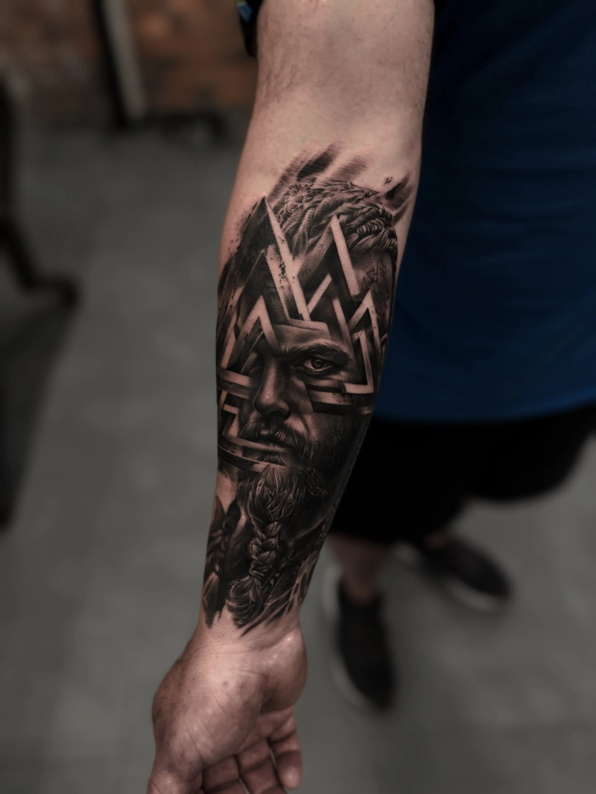 Black and grey realism Viking portrait tattoo with Valknut symbol and braided beard on forearm by Andrei Cotici at FYNE Leeds