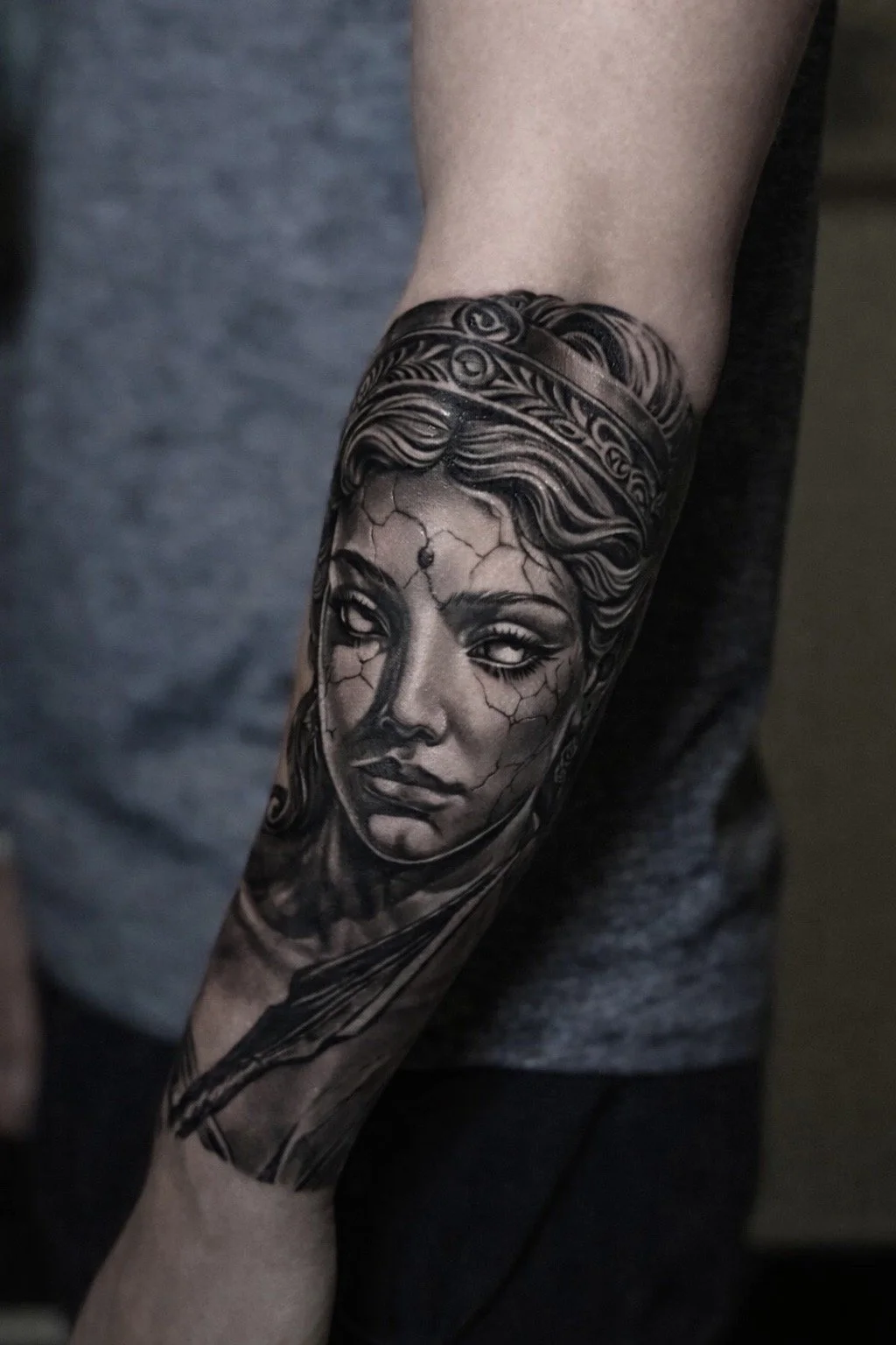 Black and grey realism tattoo of a cracked porcelain-style female portrait on forearm by Andrei Cotici at FYNE Leeds